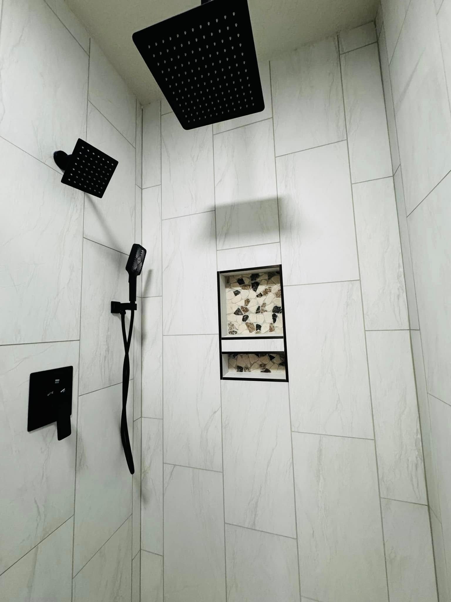 Modern shower with black fixtures, white tiled walls, and a built-in shelf with decorative tiles.