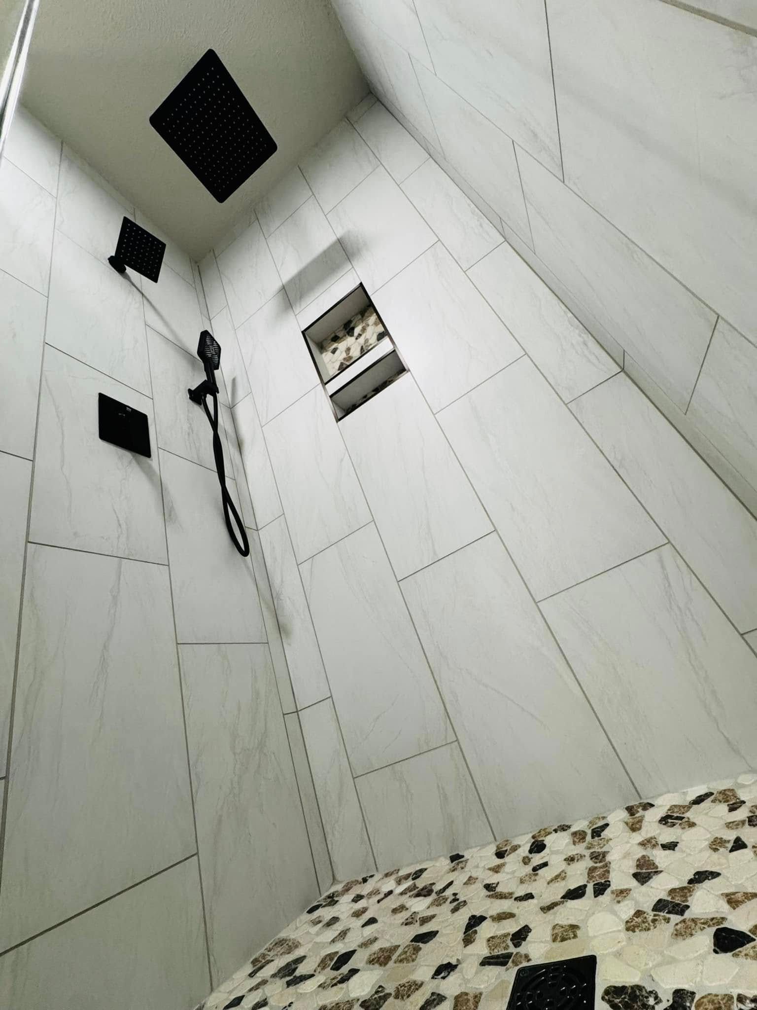 White-tiled shower with black fixtures, including a showerhead and shelving, a mosaic-tiled seat.