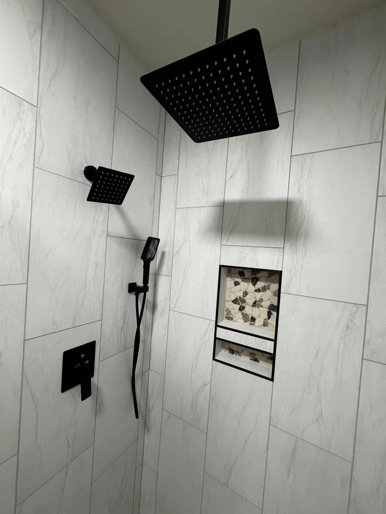 Black shower fixtures in a tiled shower niche with contrasting tile detail.