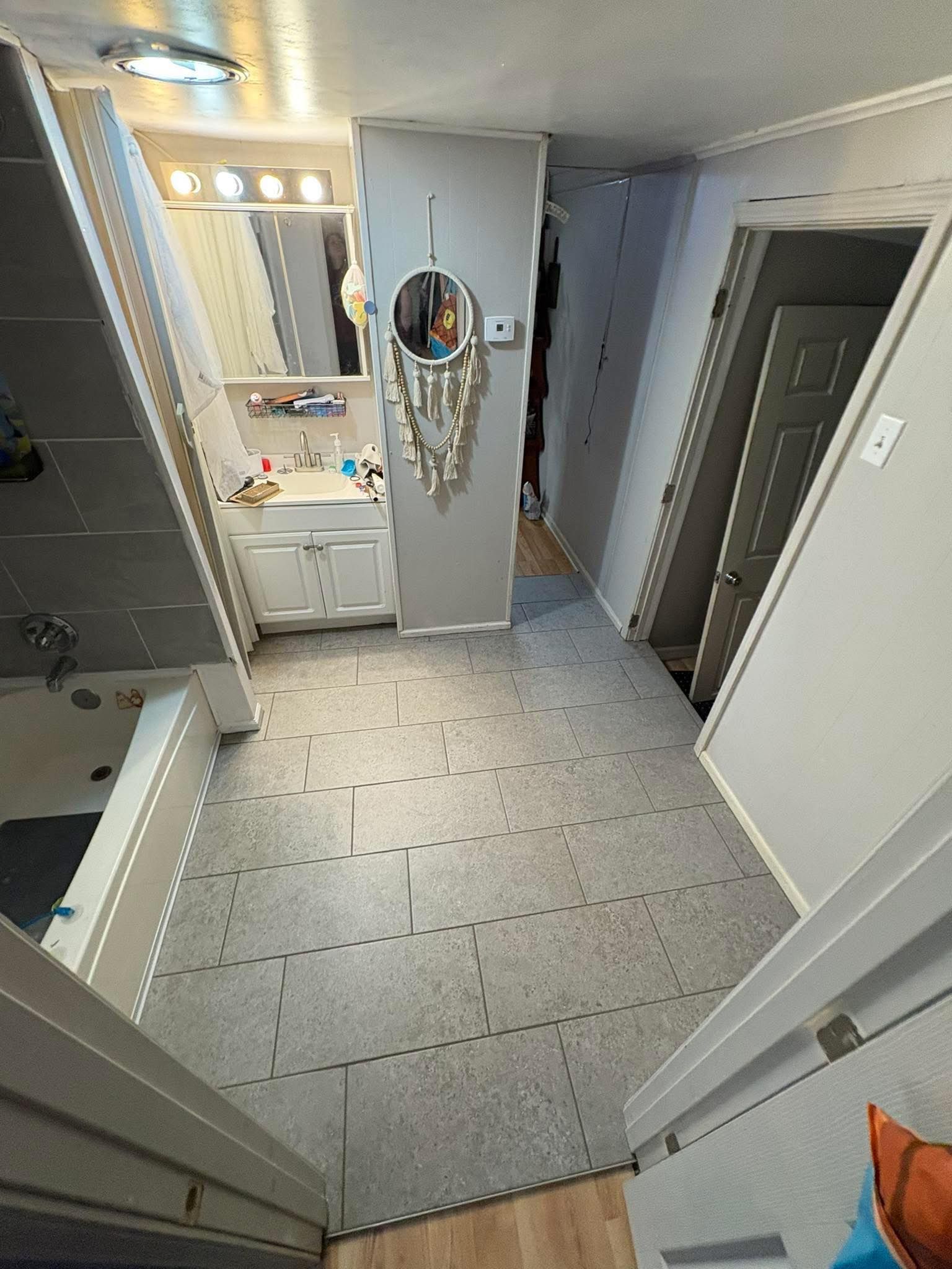 Narrow hallway with gray interlocking floor tiles, leading to bathroom with vanity and tub.