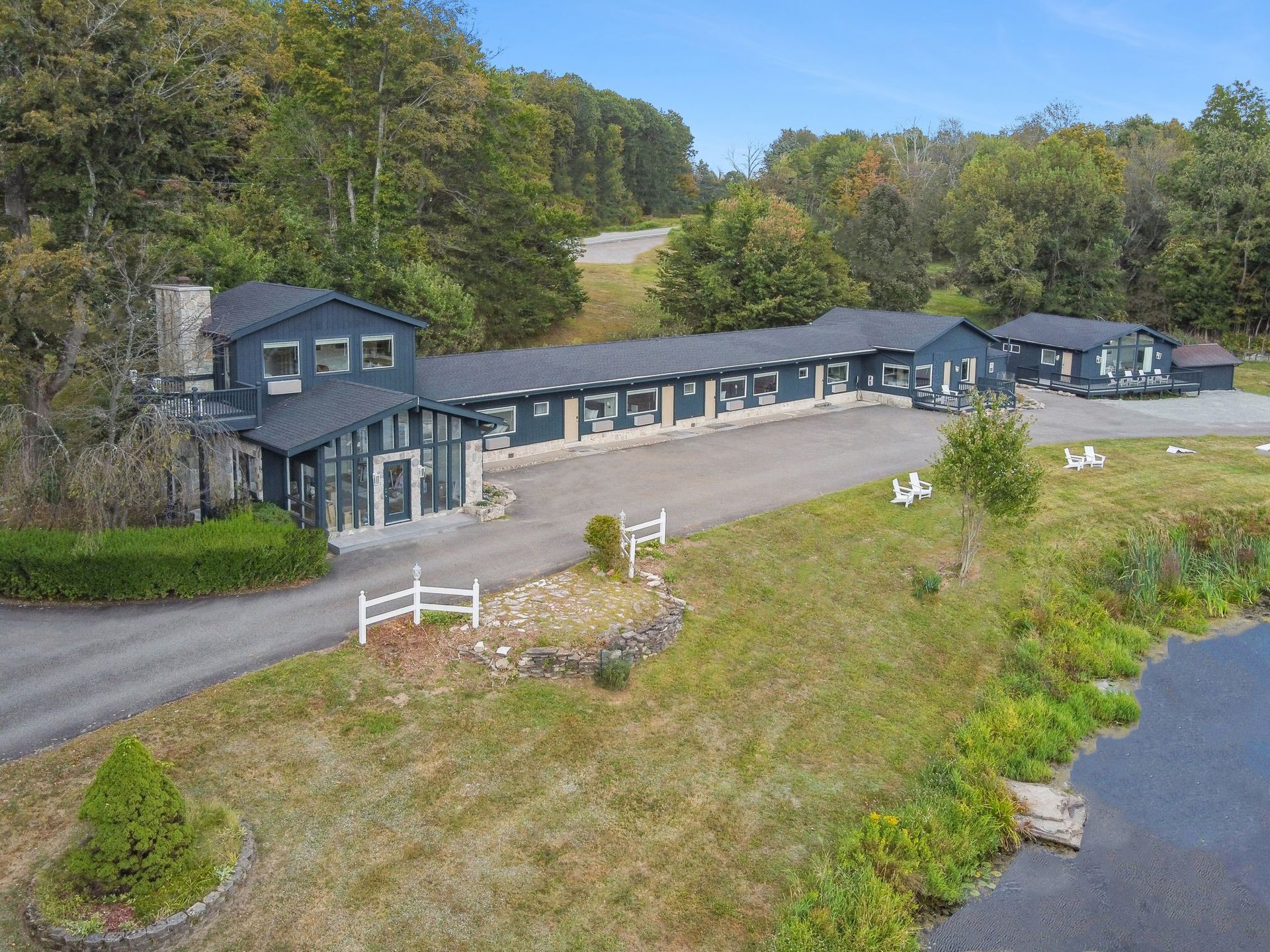 Dark blue building nestled among trees, with a driveway and grassy area.