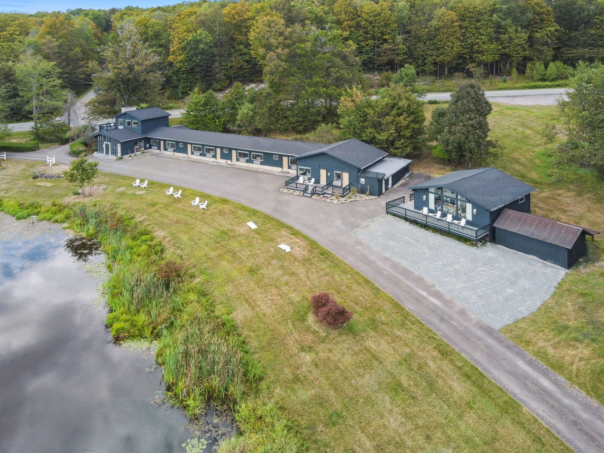 Aerial view of a blue motel with a long driveway, next to a lake with geese.