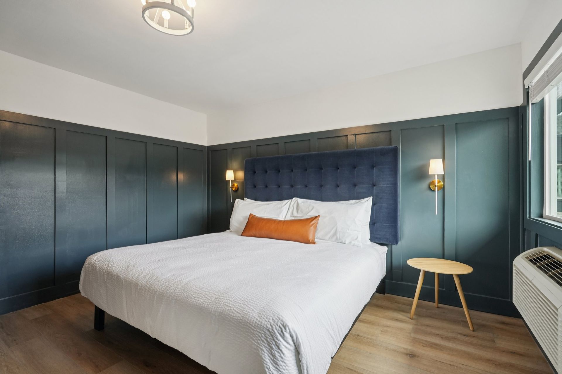 Bedroom with blue paneling, a bed, small table, and window.
