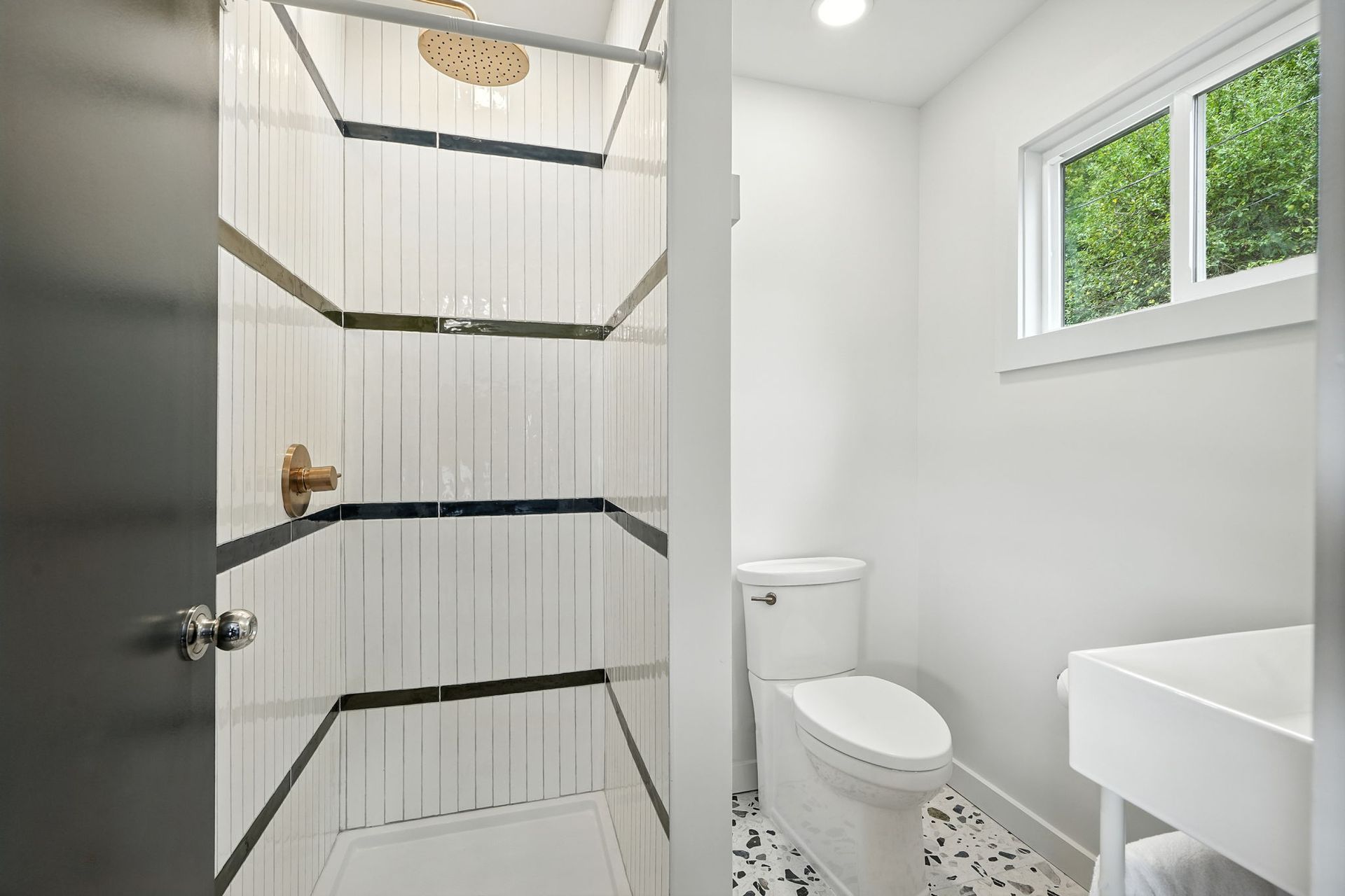 Modern bathroom with white walls, hexagon-tiled shower, toilet, and window.
