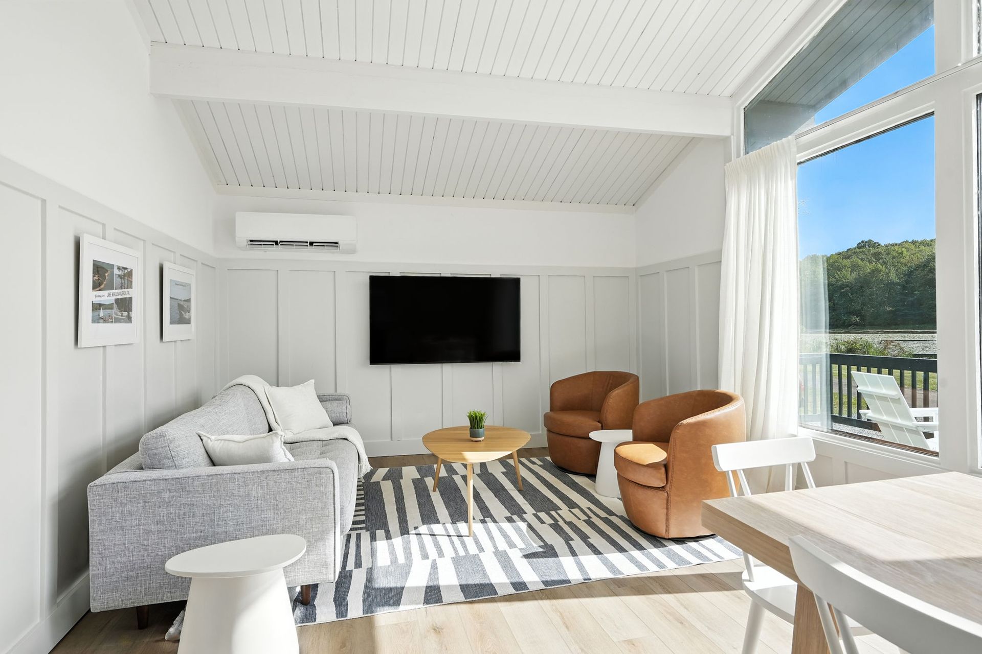 Bright living room with sofa, chairs, TV, and a view of a lake.