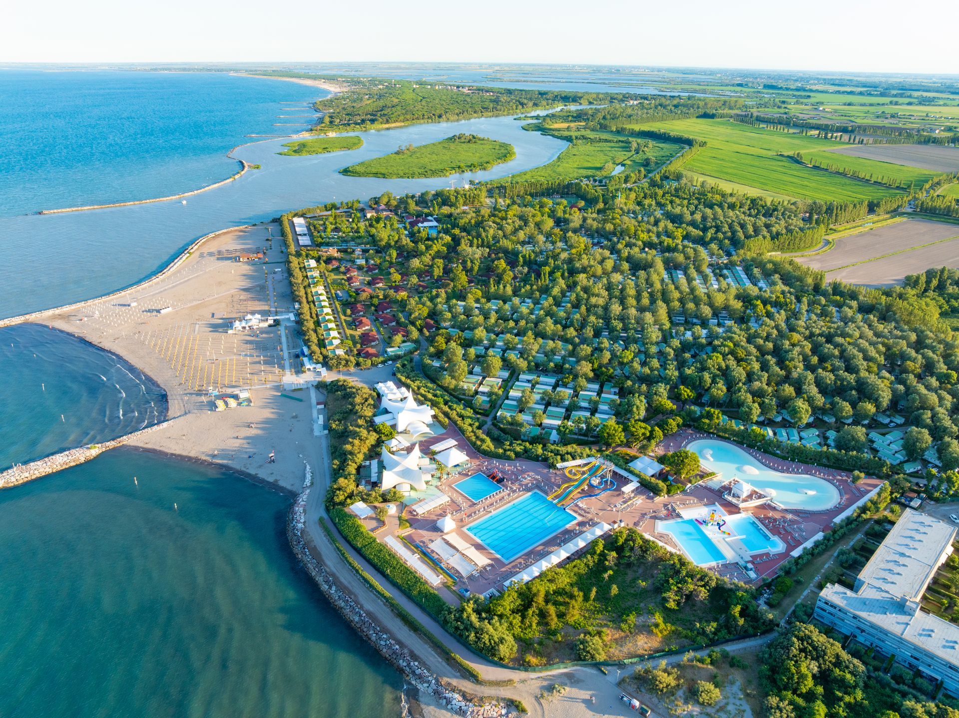 Aerial view of a resort with a pool complex, beach, and lagoon next to the sea.
