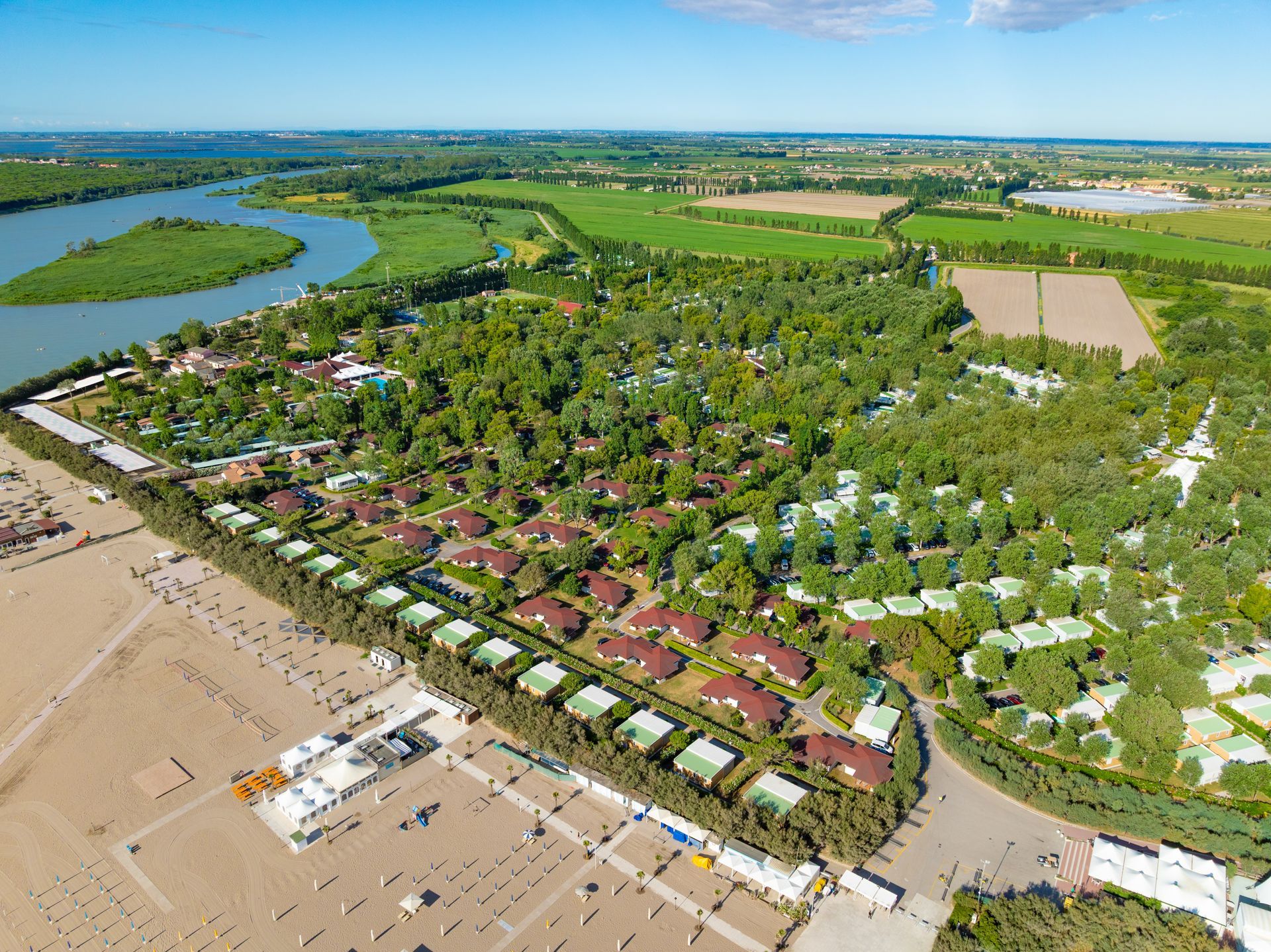Vista aerea di un grande campeggio con cabine, alberi, un fiume e campi.