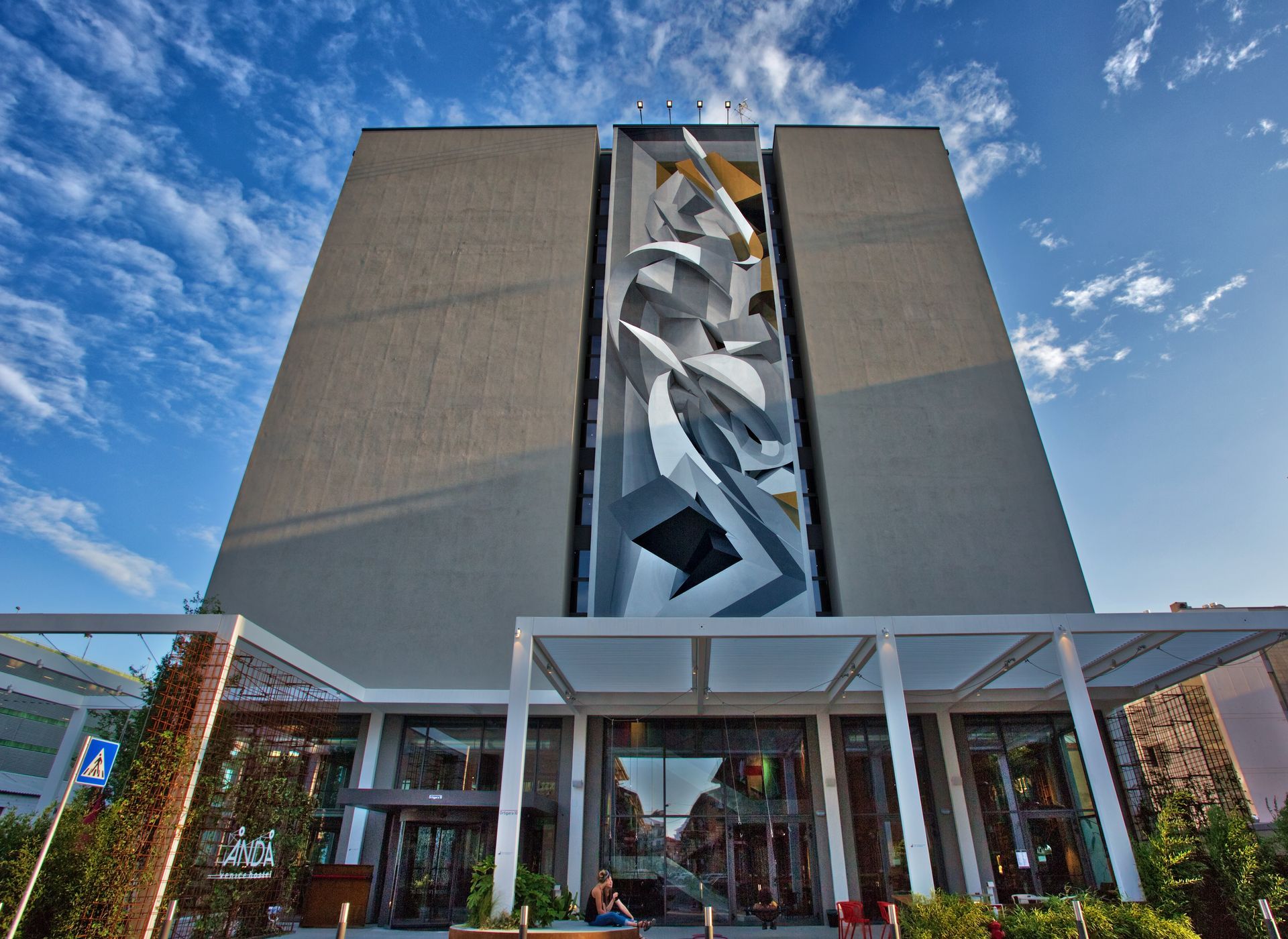 A tall, gray building with a large abstract mural; a modern entrance below, blue sky above.