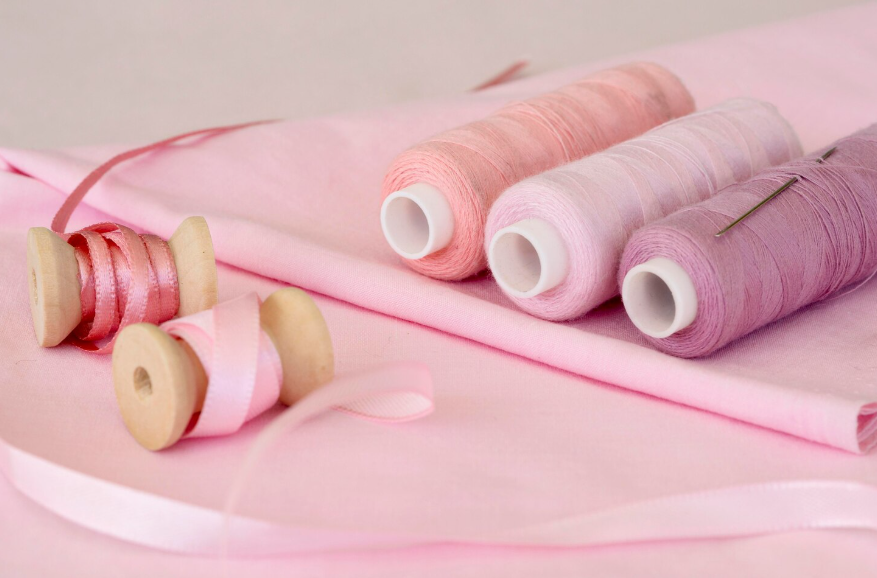 Carretes de hilo y cinta de color rosa sobre tela rosa, con aguja.