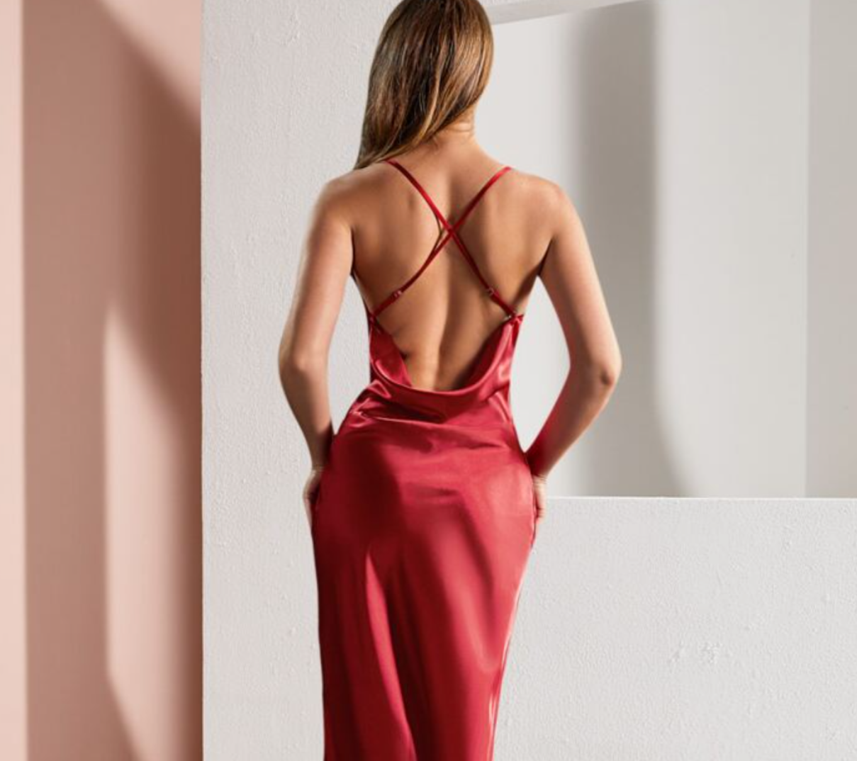 Mujer con vestido de seda roja con tirantes cruzados y manos en los bolsillos.