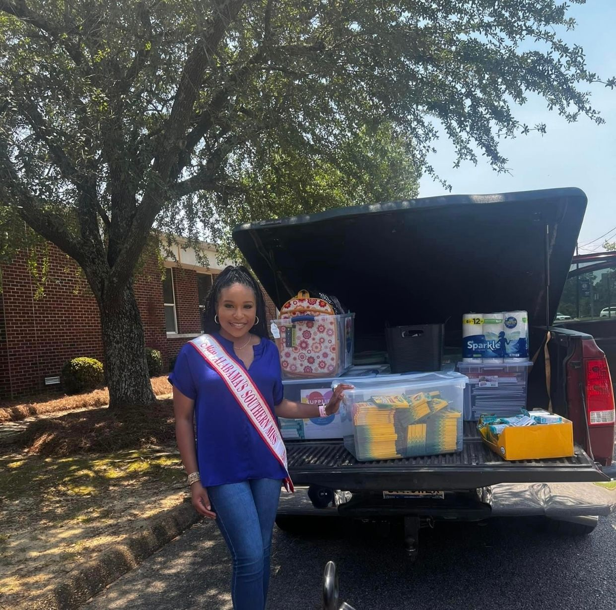 A woman wearing a sash that says miss texas is standing in front of a truck