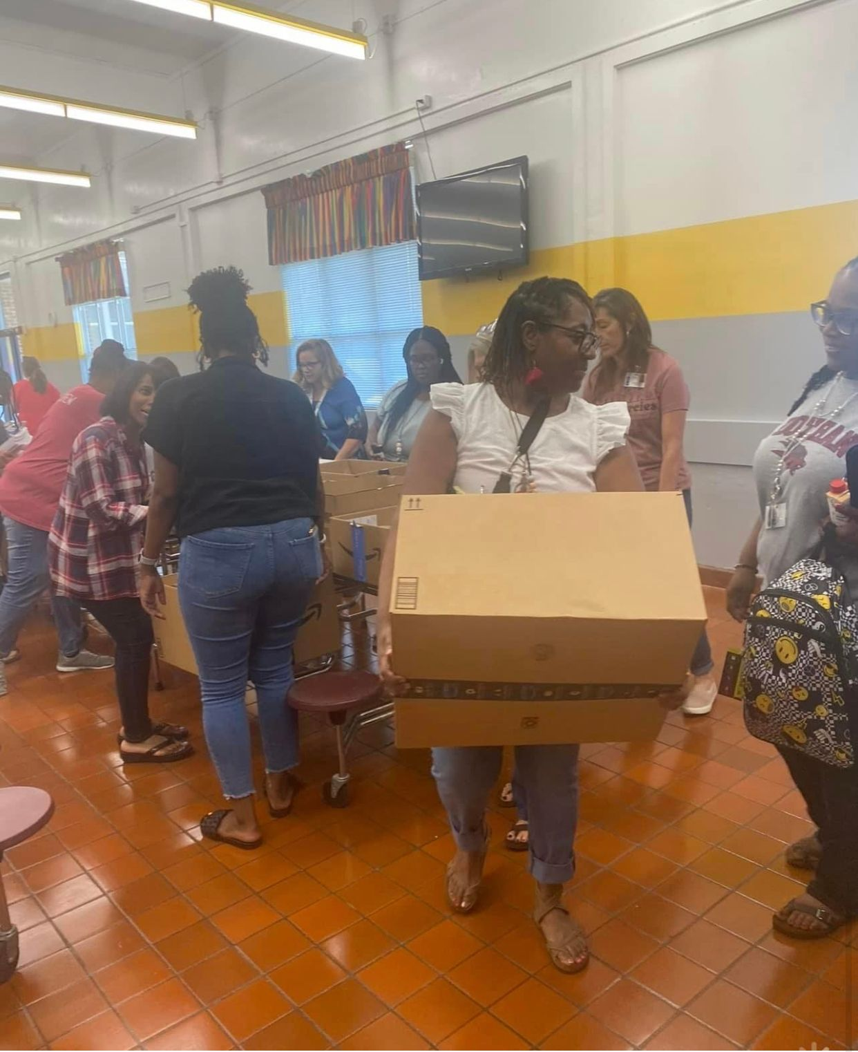 A woman is carrying a large cardboard box in a room.