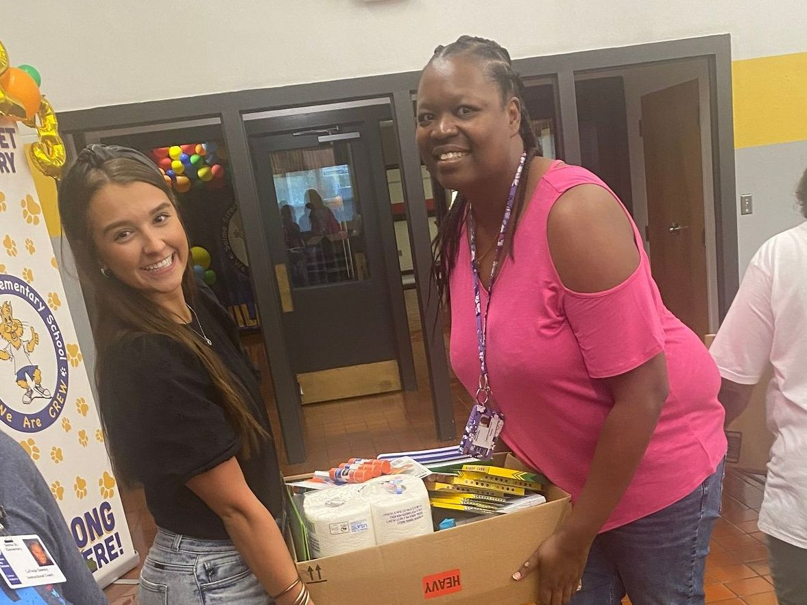 A woman in a pink shirt is holding a box of toilet paper.