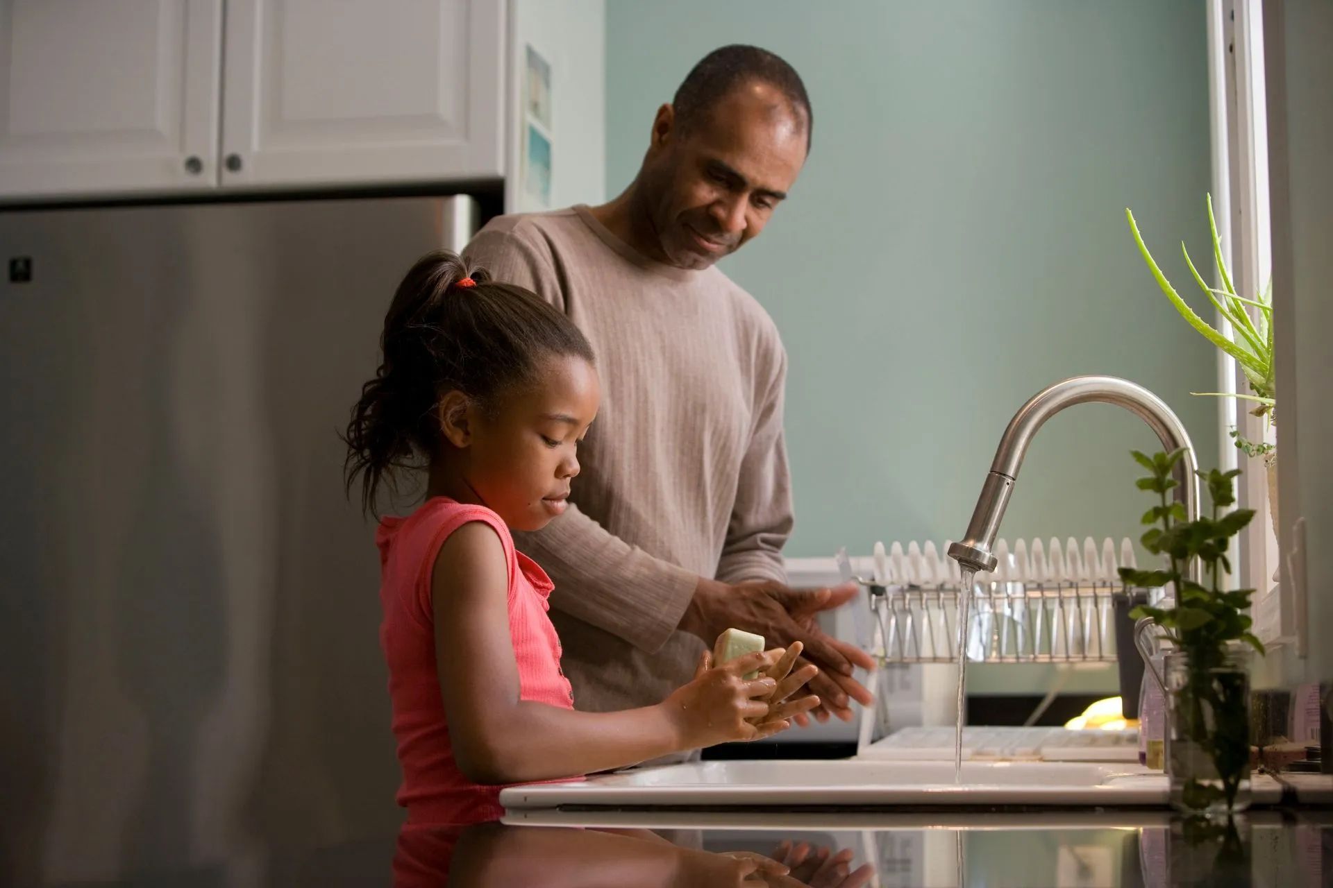 A man and a little girl are washing their hands in a kitchen sink.