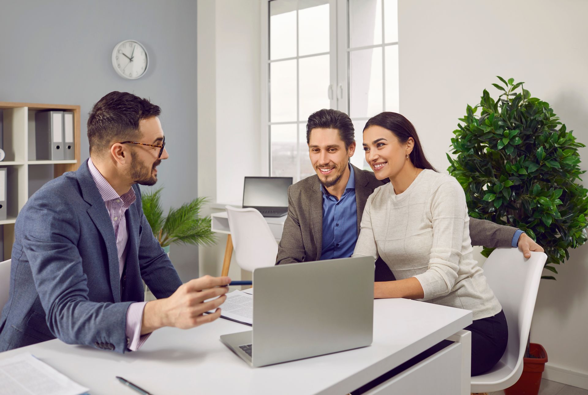 A man is talking to a couple while sitting at a desk with a laptop.