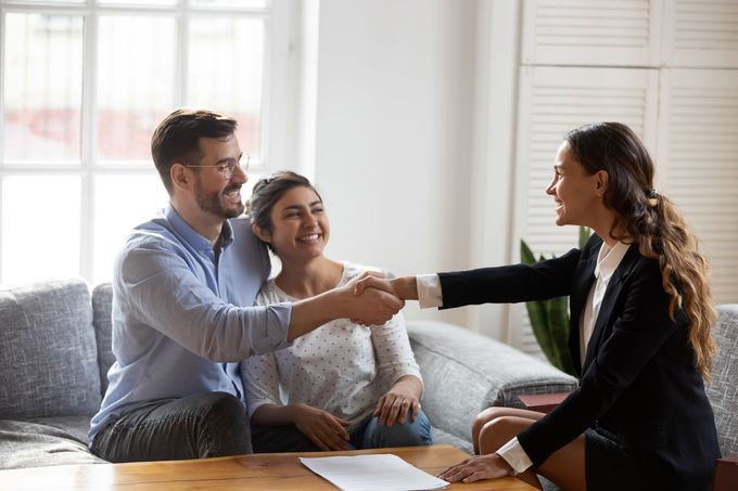 A man and woman are shaking hands with a real estate agent while sitting on a couch.