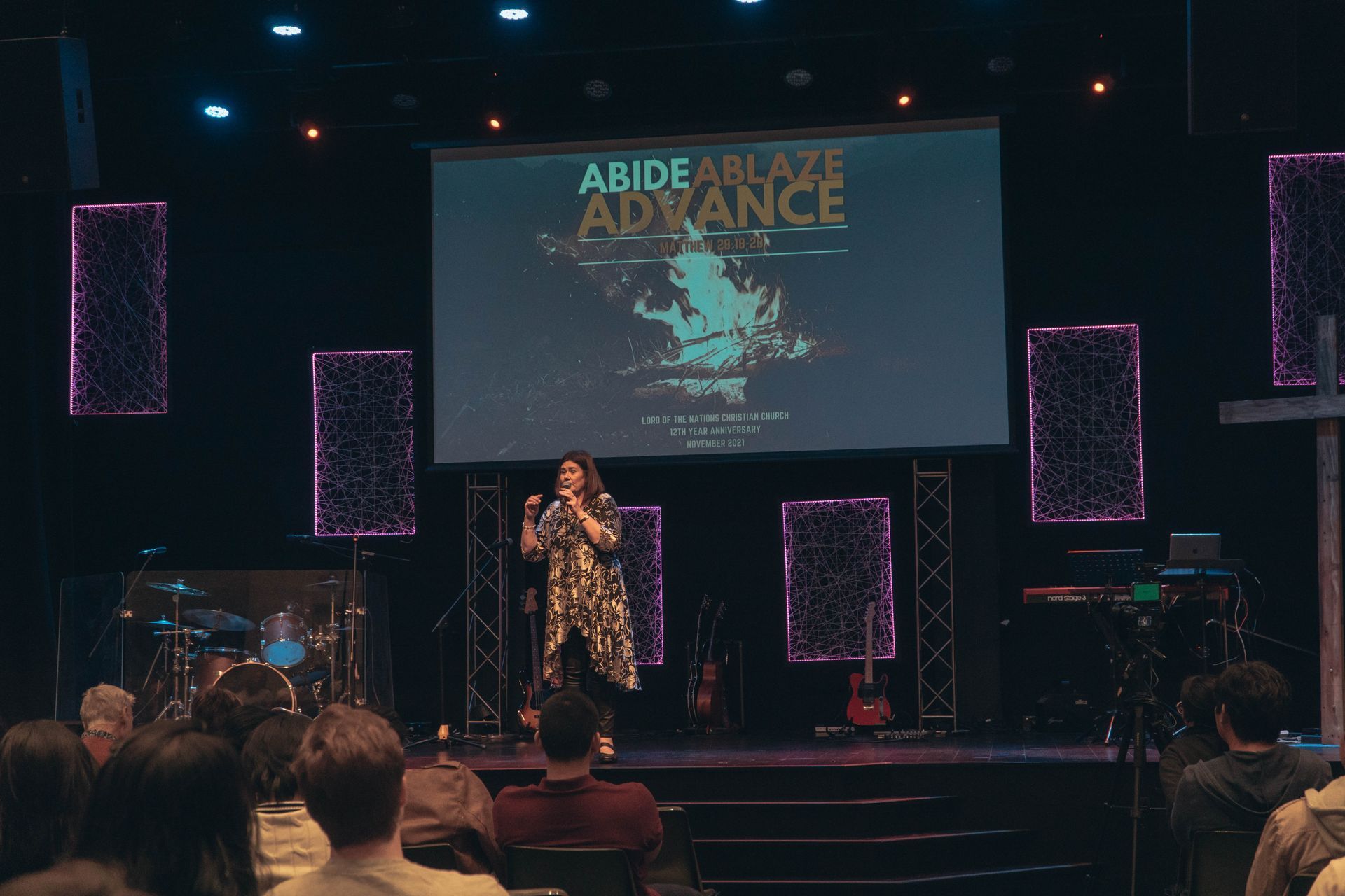 Woman speaking on stage with a screen that says
