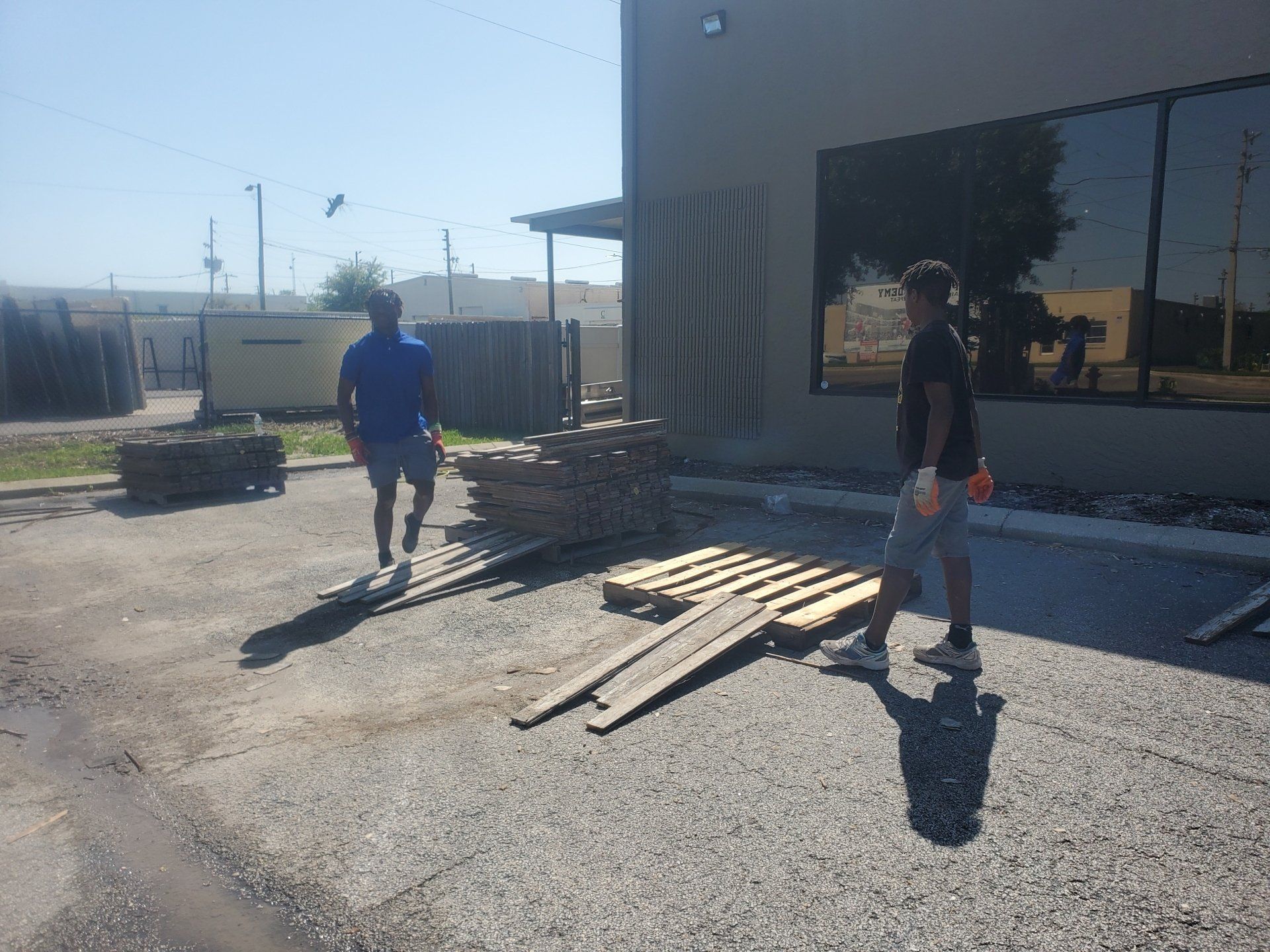 Two men are walking in a parking lot with wooden pallets in front of a building.