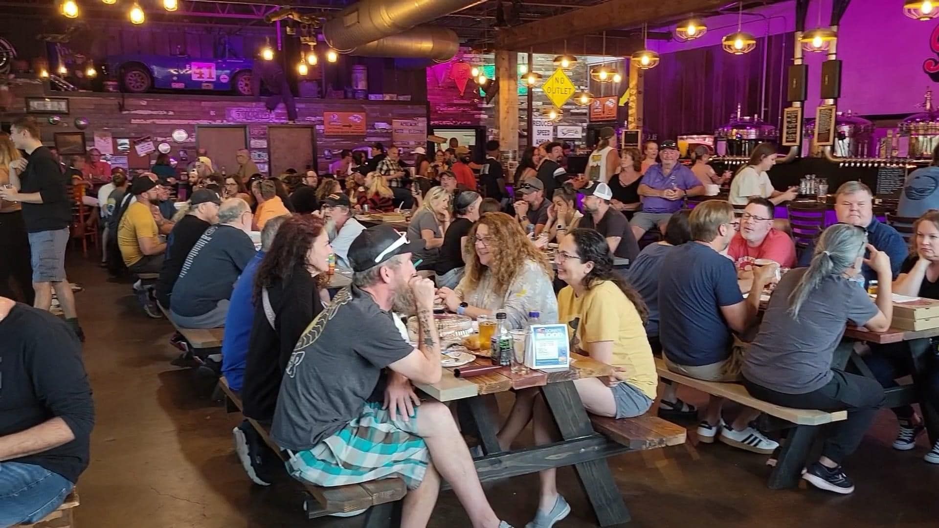 A large group of people are sitting at picnic tables in a restaurant.