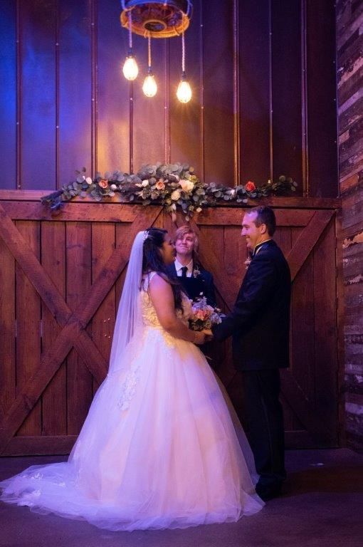 A bride and groom are kissing during their wedding ceremony in a barn.