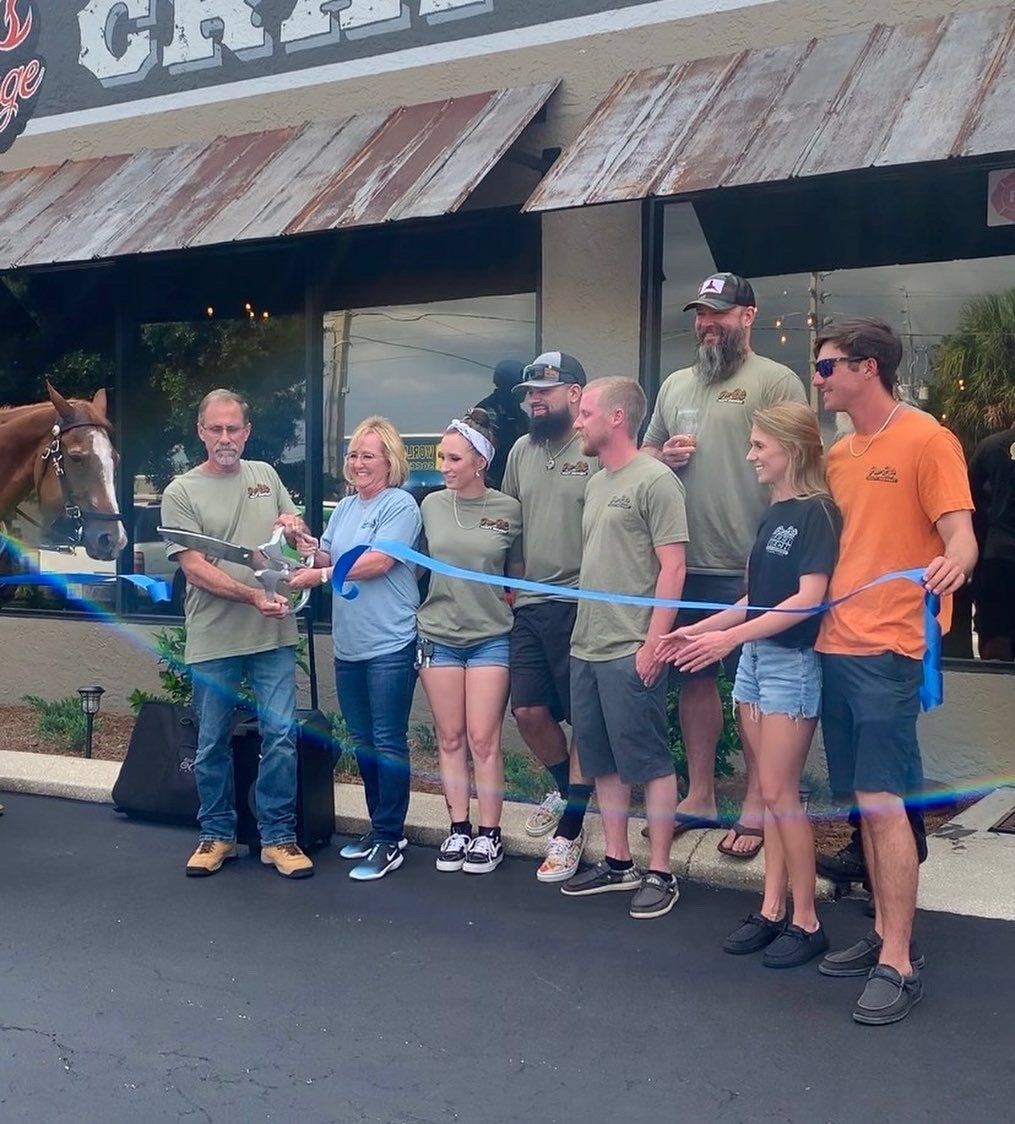 A group of people cutting a blue ribbon in front of a restaurant