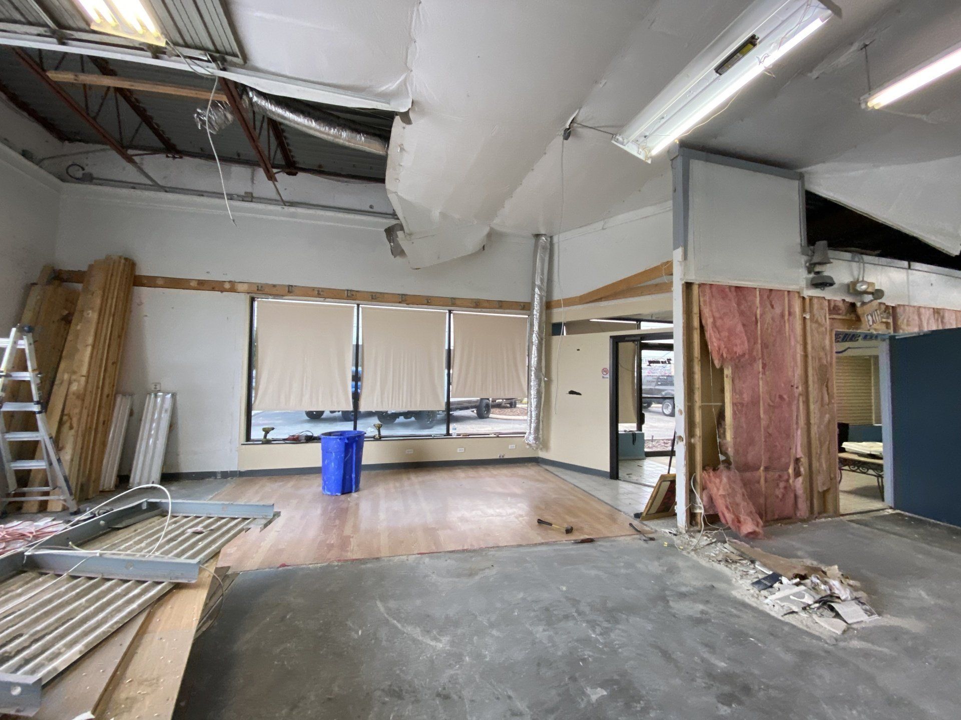 An empty room with a blue trash can in the middle of it.