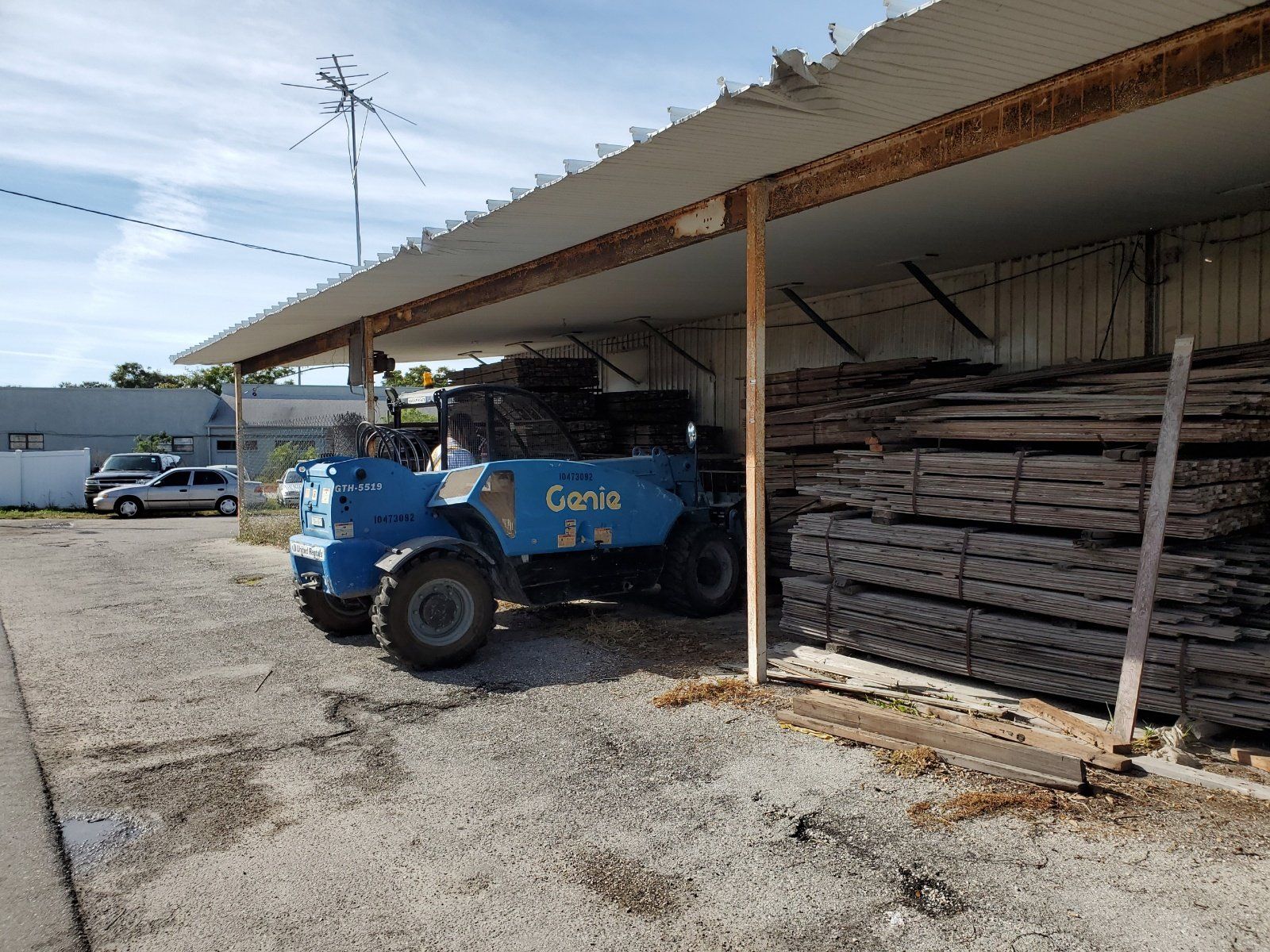 A blue forklift is parked in front of a building next to a pile of wood.