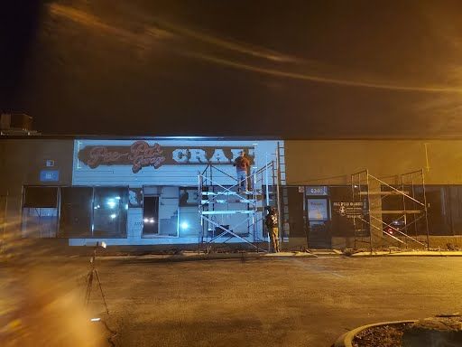 A man is painting a sign on the side of a building at night.