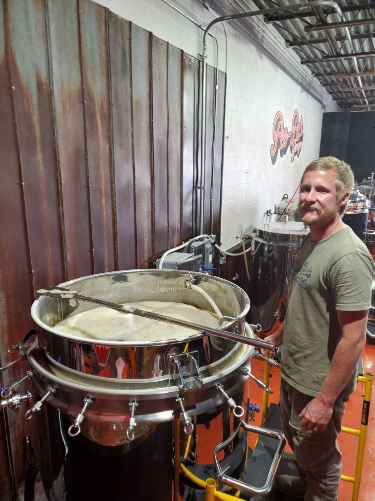 A man is standing in front of a large pot of liquid.