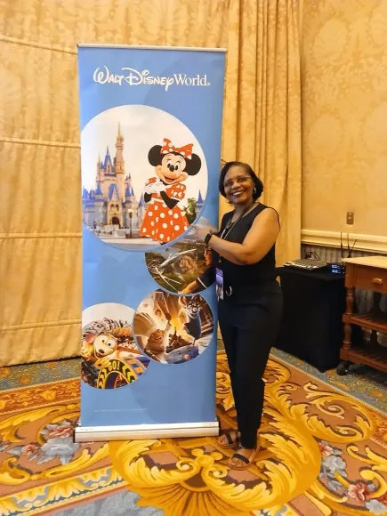 Woman stands next to a Walt Disney World banner featuring Minnie Mouse and Cinderella Castle. She holds a gift basket.