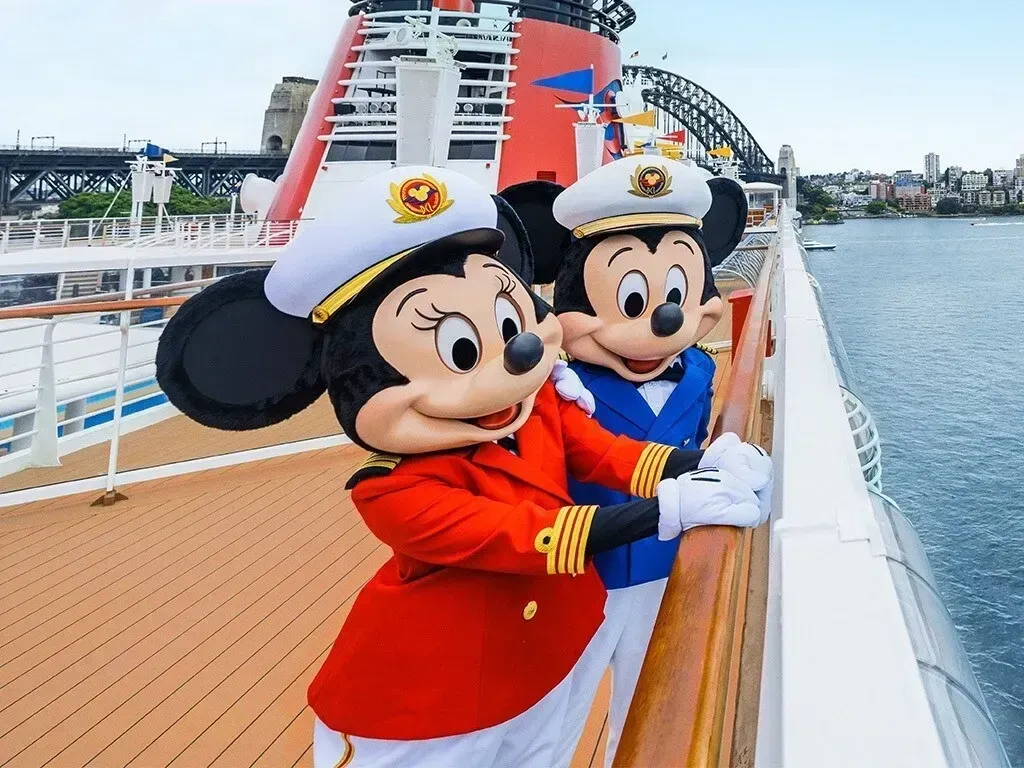 Mickey and Minnie Mouse dressed as ship captains, posing on a cruise ship deck in front of Sydney Harbour Bridge.