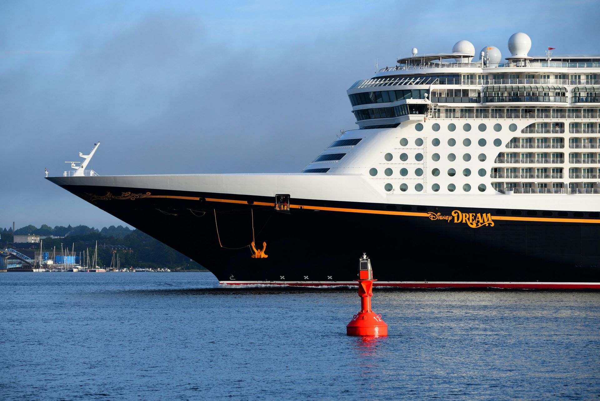 A Disney cruise ship sailing on the water with a red buoy in the foreground.
