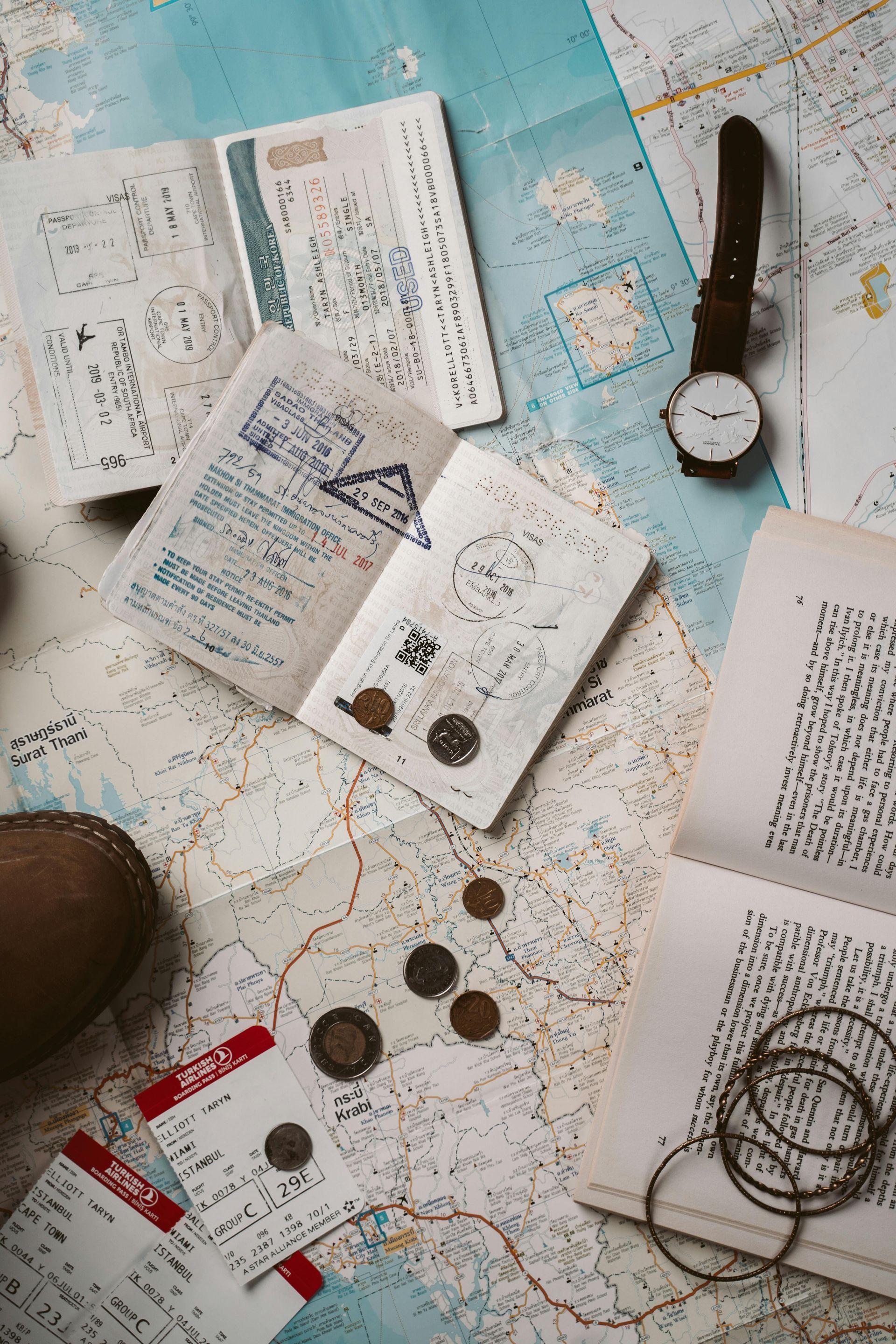Open passports, watch, tickets, coins, and bracelets scattered on a map, suggesting travel planning.