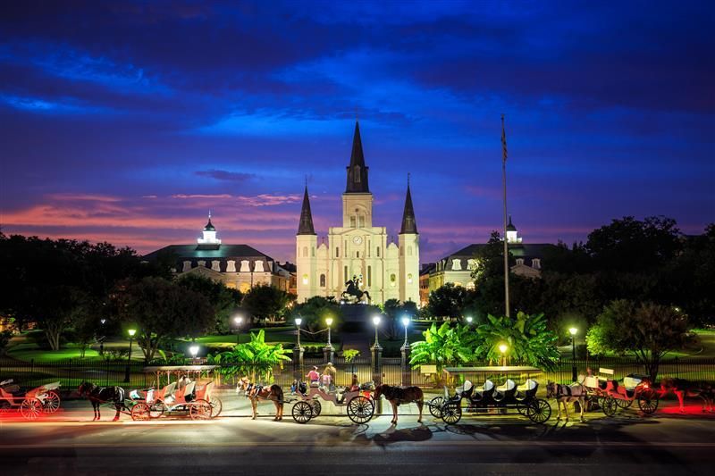 St. Louis Cathedral at dusk in New Orleans, with horse-drawn carriages and a vibrant purple and blue sky.