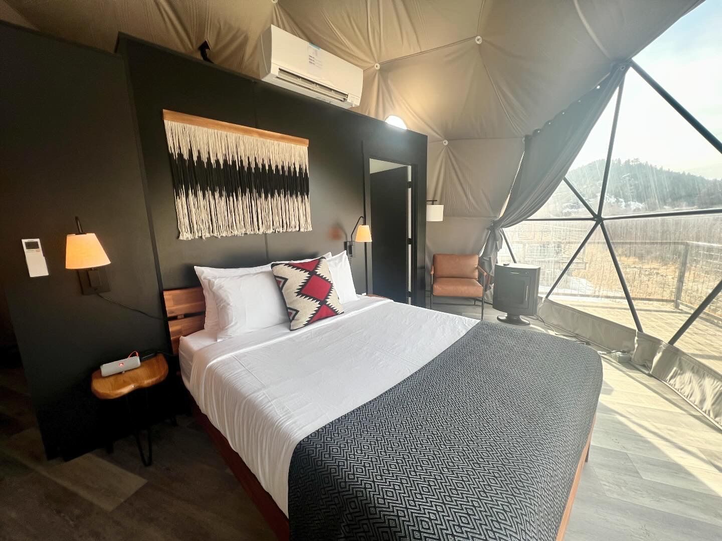 Bedroom inside a geodesic dome with bed, artwork, and a view of nature.