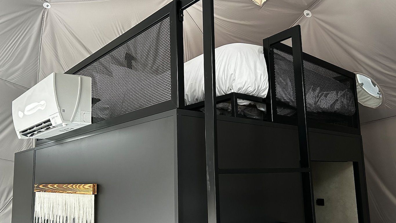 Black bunk bed inside a domed structure, with air conditioner and decorative textile.