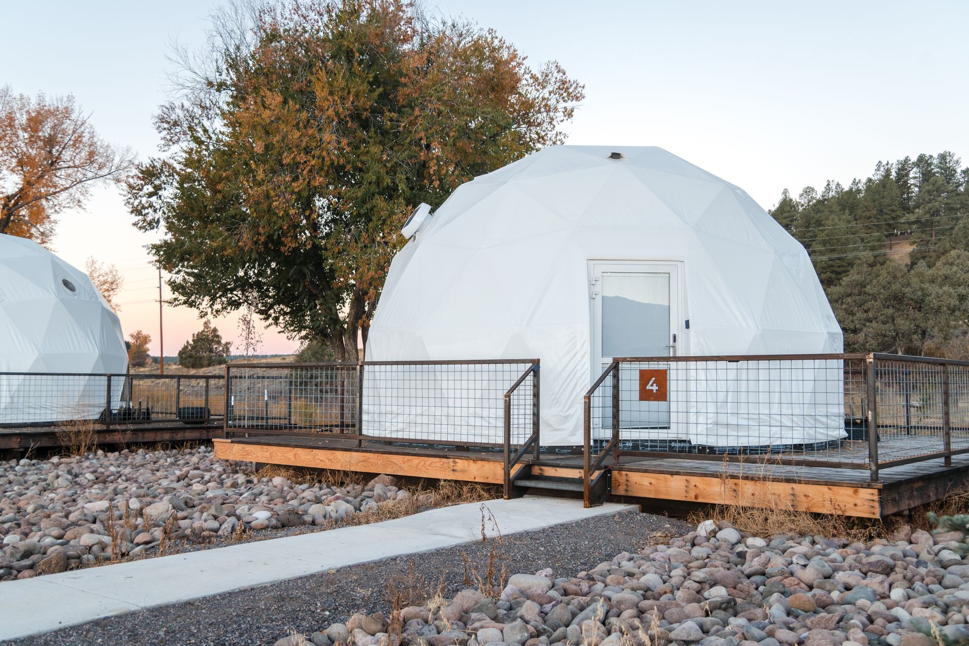 White geodesic dome glamping tents on wooden platforms, set in a rocky landscape with trees.