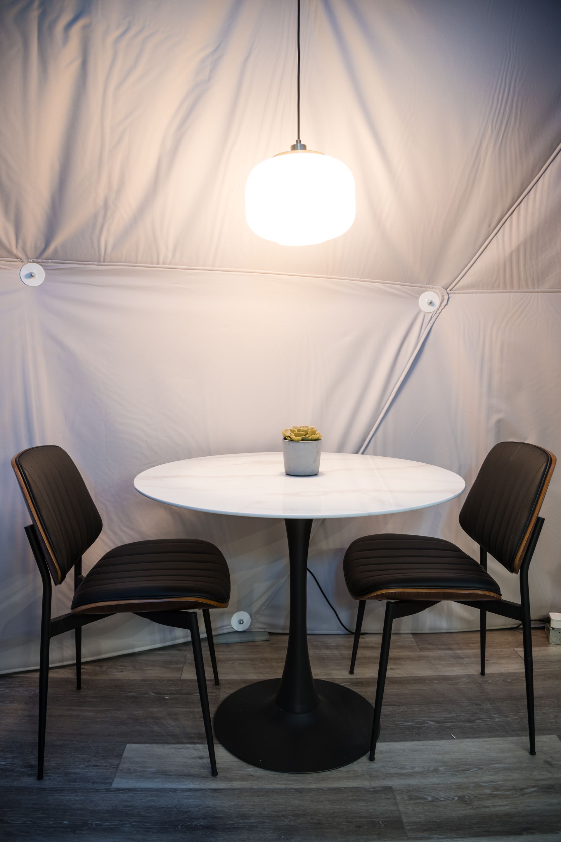 Round table with two chairs under a pendant light in a dome structure.