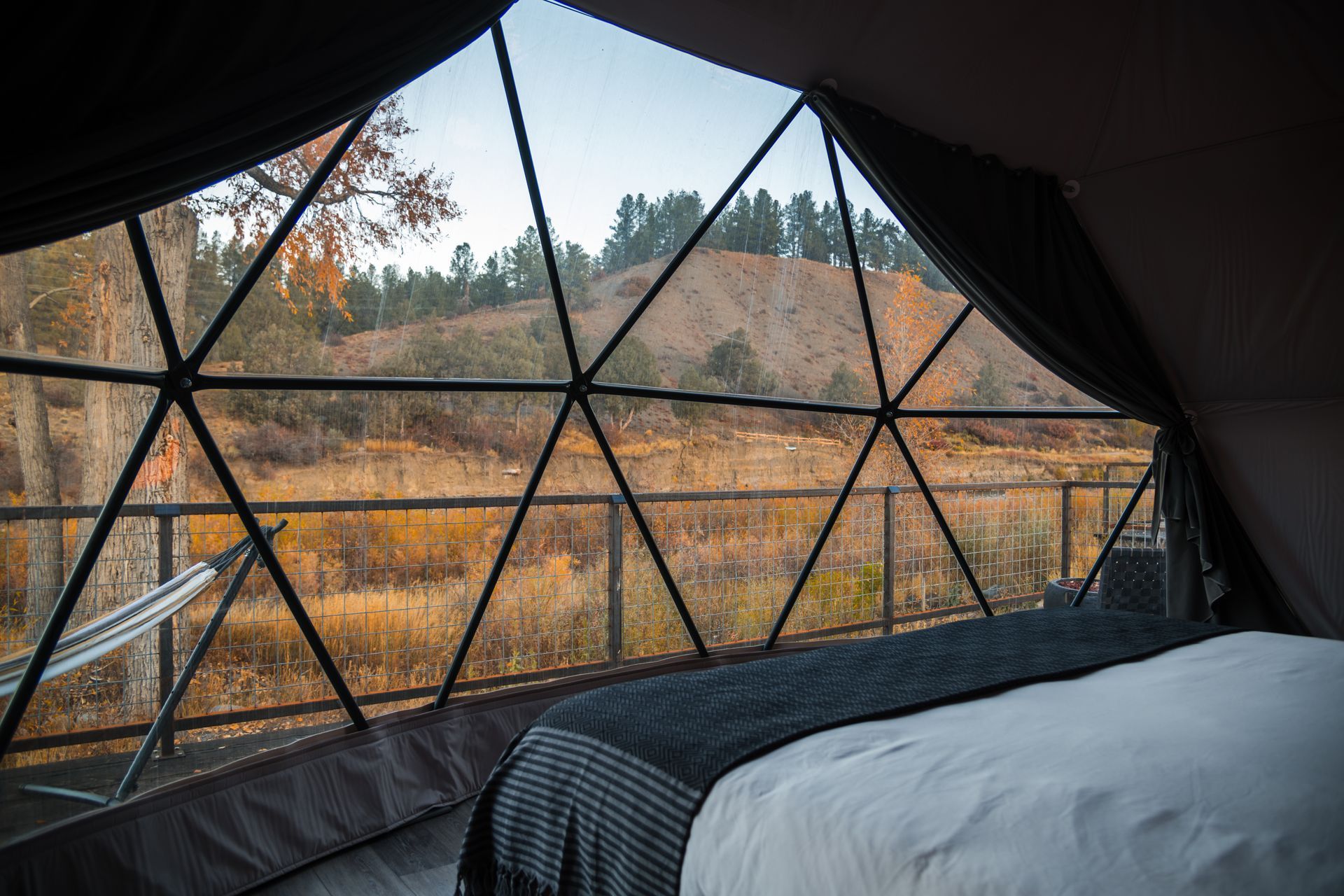 View from a dome-shaped tent with a bed looking onto a grassy field and hillside.
