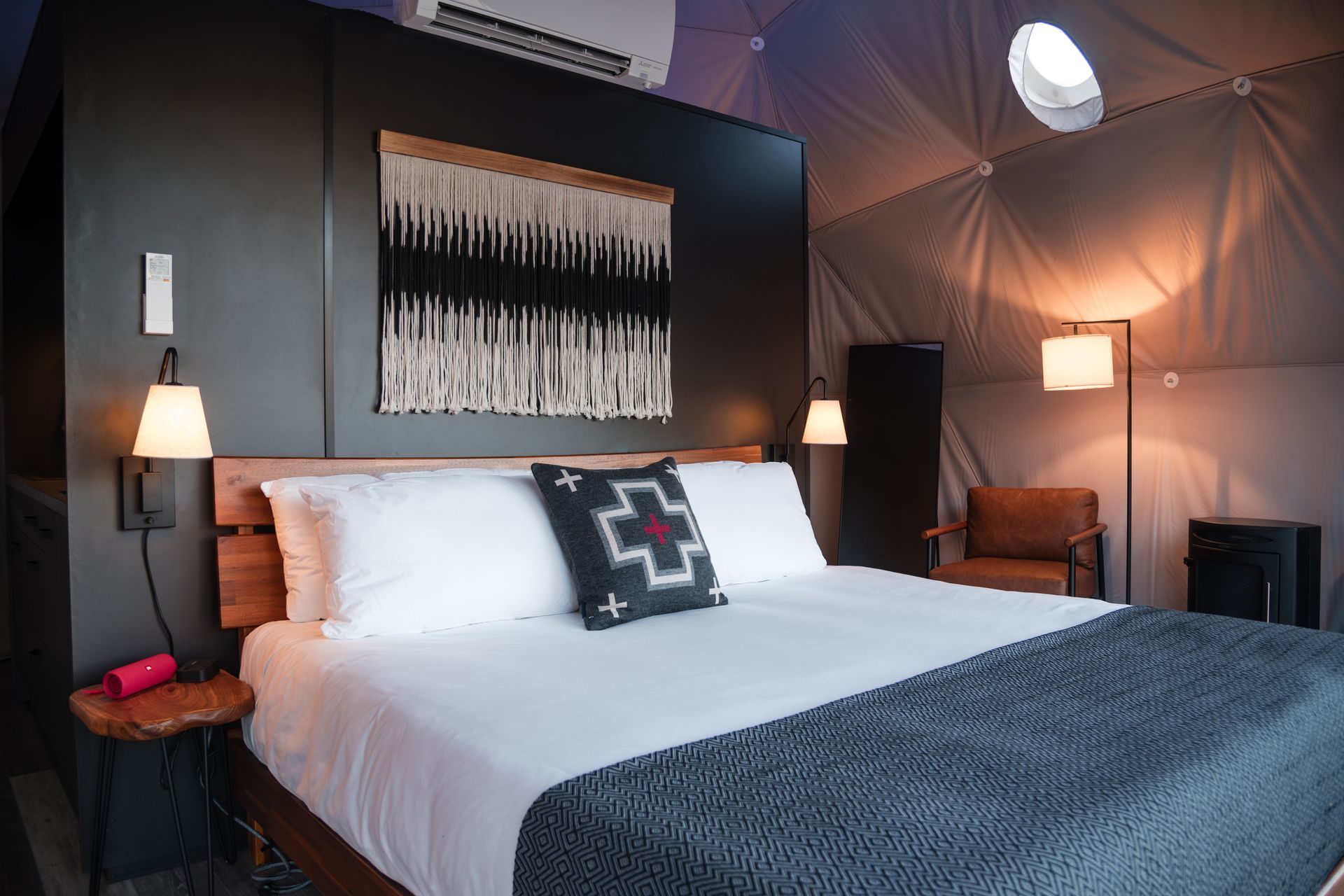 Bedroom inside a geodesic dome, with a bed, decorative wall hanging, and a sitting area.