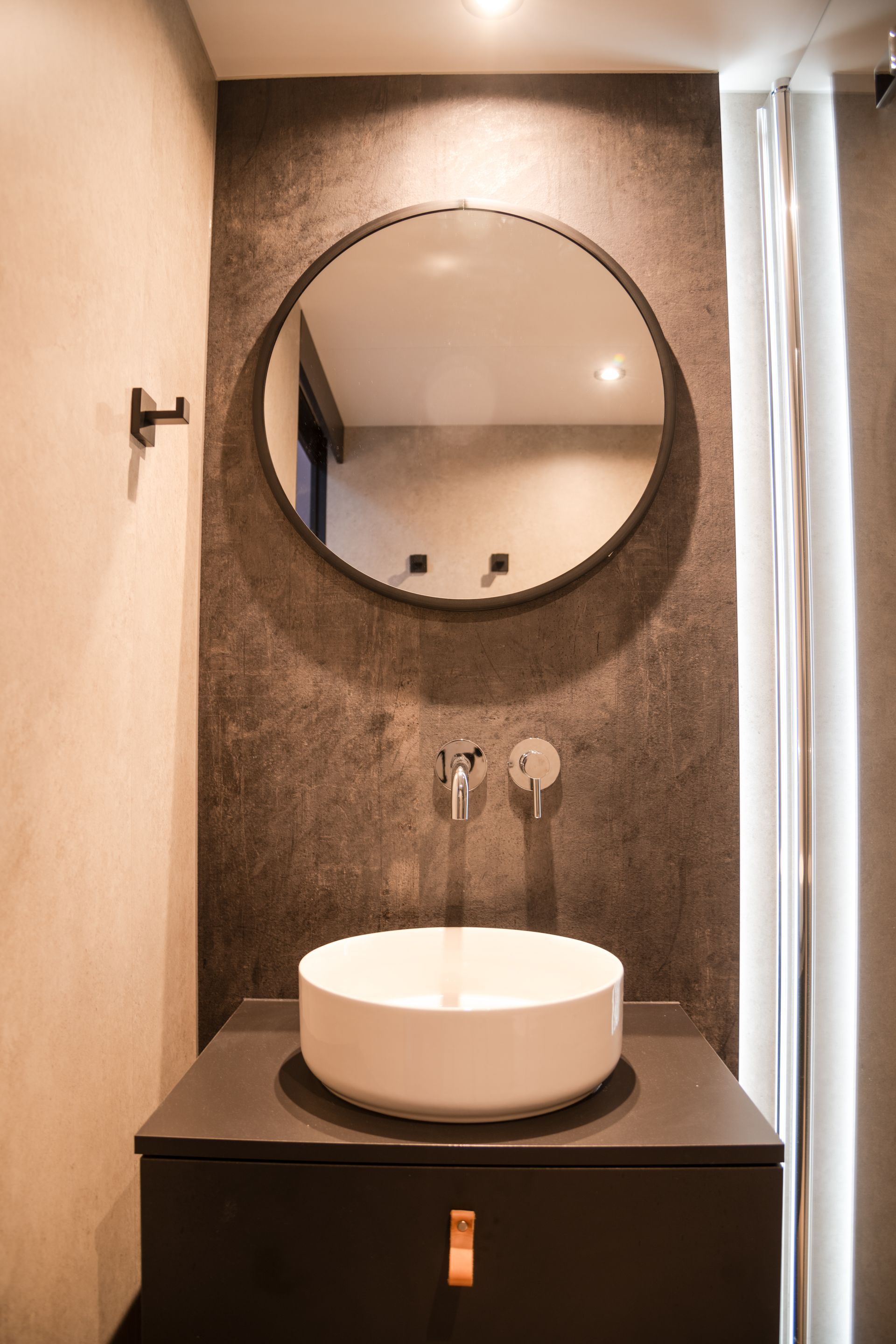 Modern bathroom with a round mirror over a white sink and gray cabinet.
