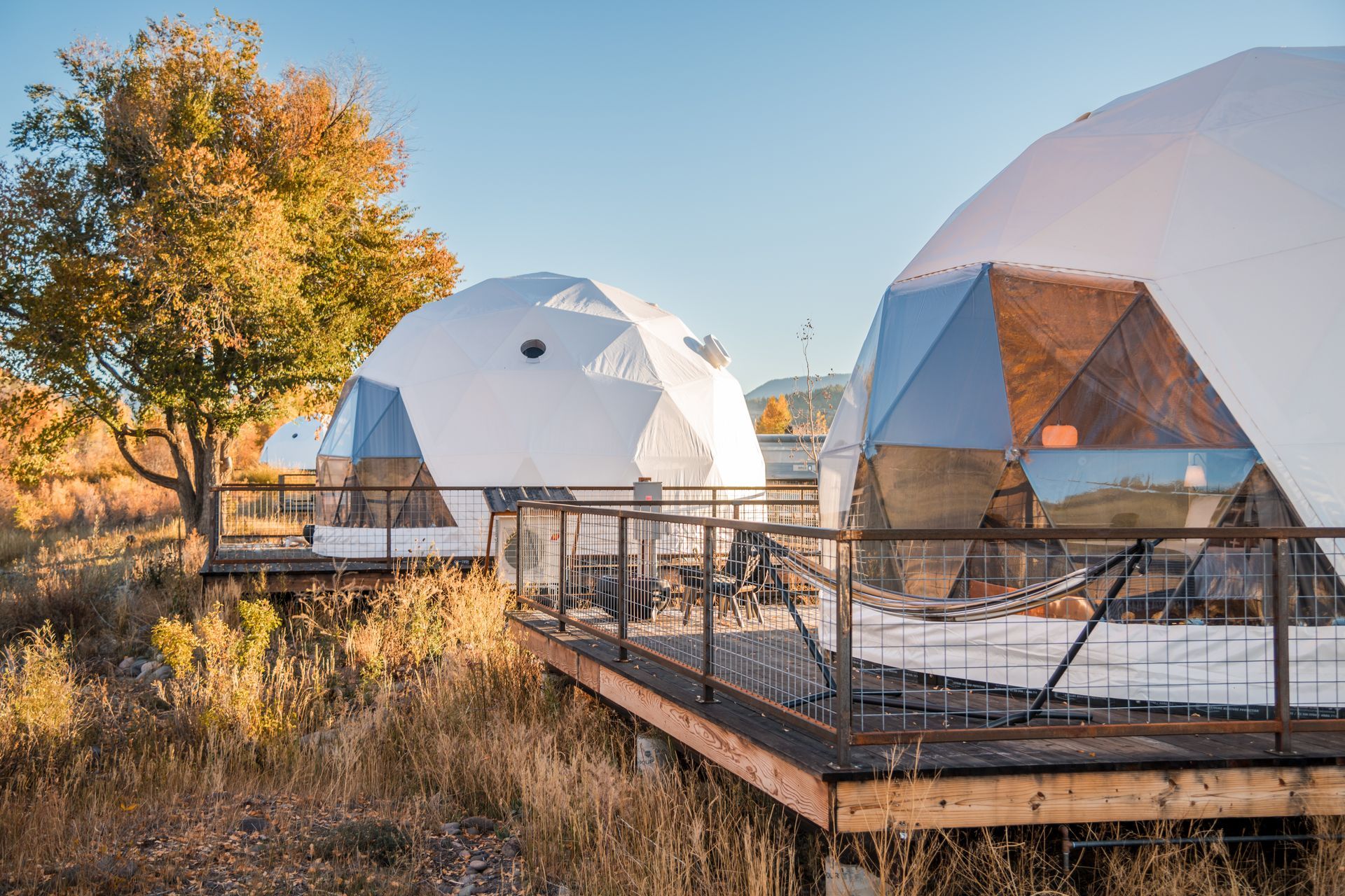 Two white geodesic dome structures on wooden platforms in a field under a clear sky.