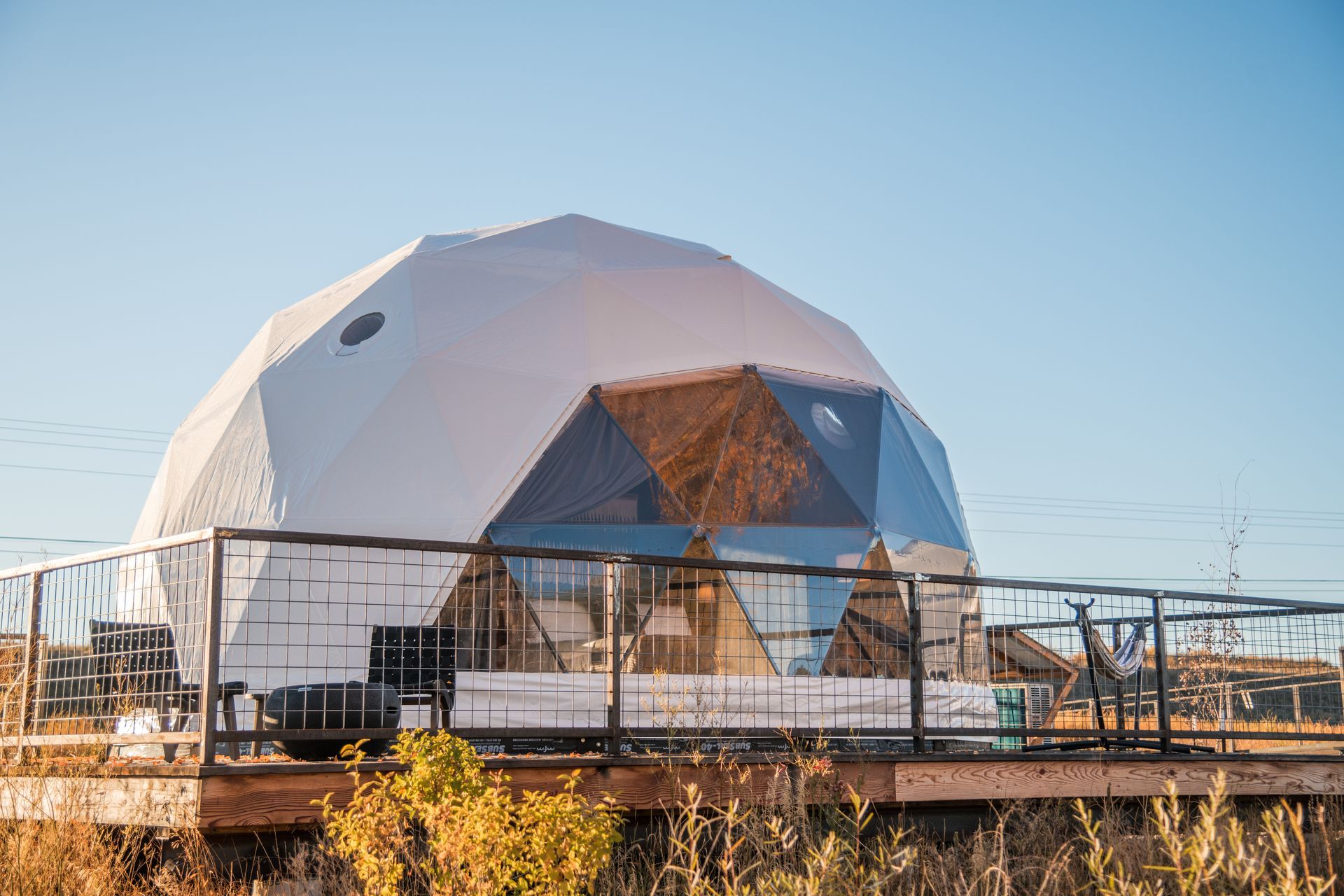 Geodesic dome-shaped structure with a deck, set against a clear blue sky and dry landscape.