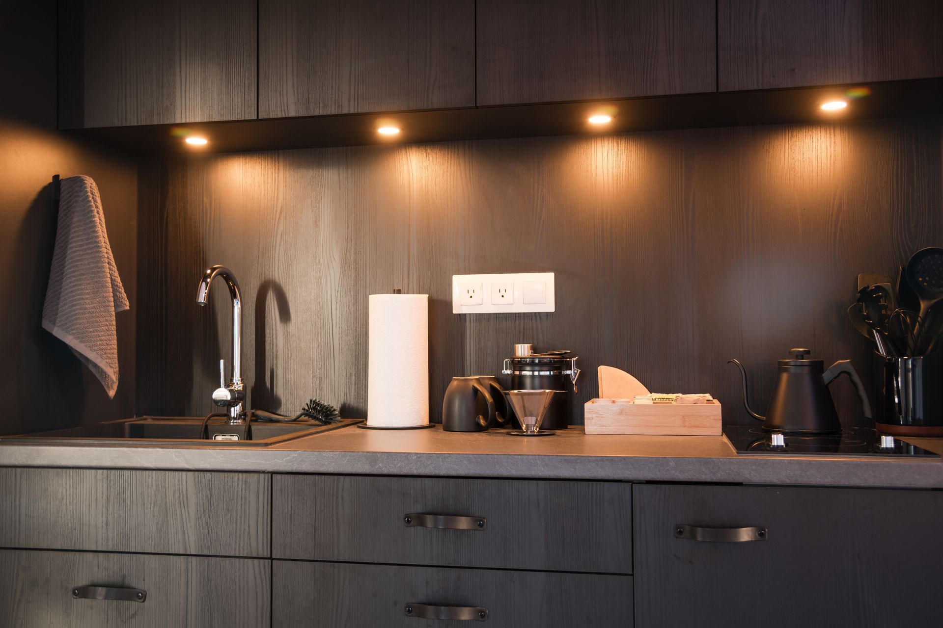 Kitchen with wooden cabinets, countertops, and under-cabinet lighting. Items include a faucet, paper towels, and a coffee grinder.