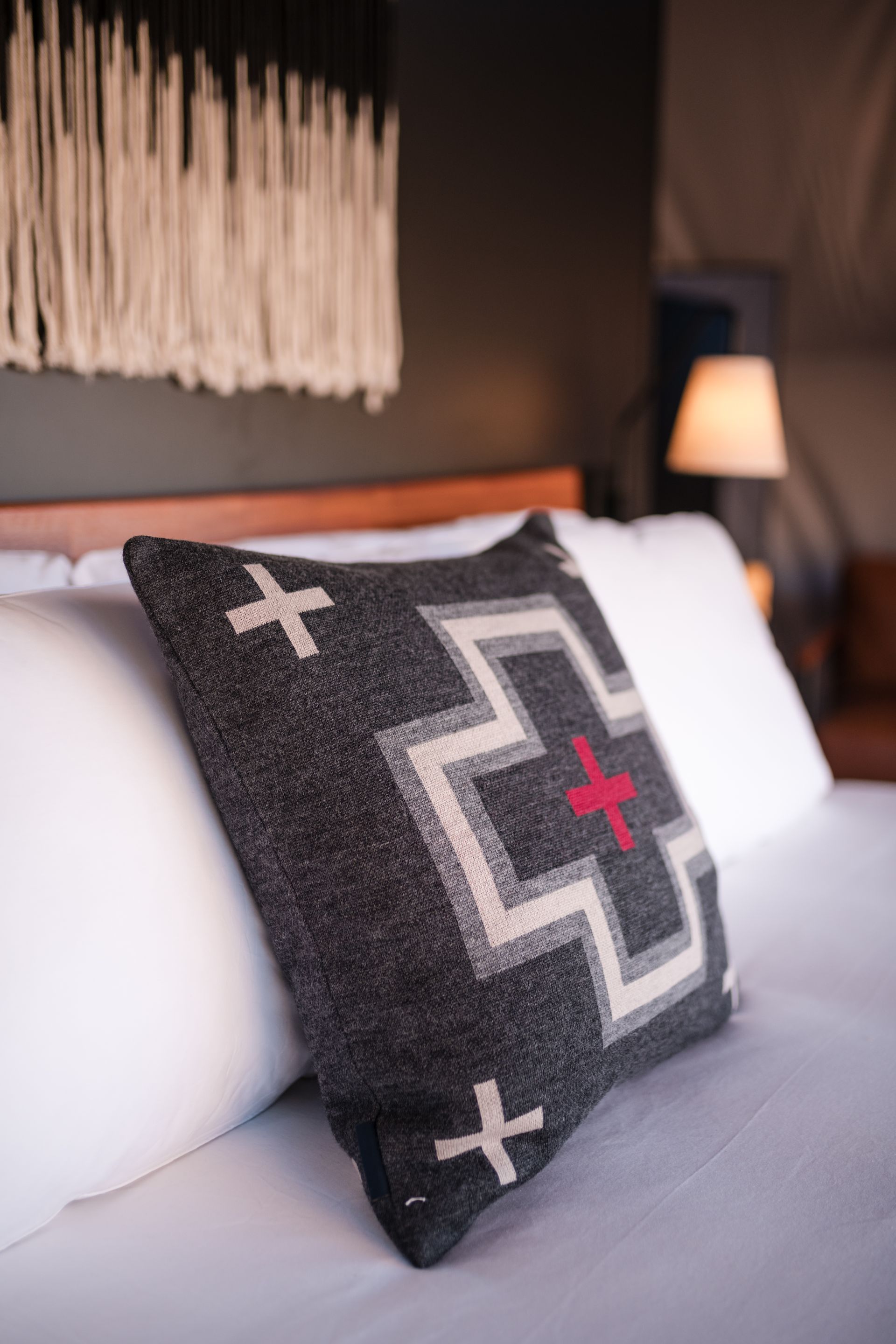Bed with decorative pillows. Gray and white patterned pillow. White pillows, wooden headboard.