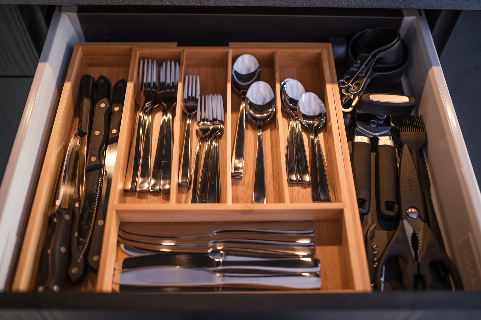 Cutlery organized in a wooden drawer, including forks, spoons, knives, and serving utensils.