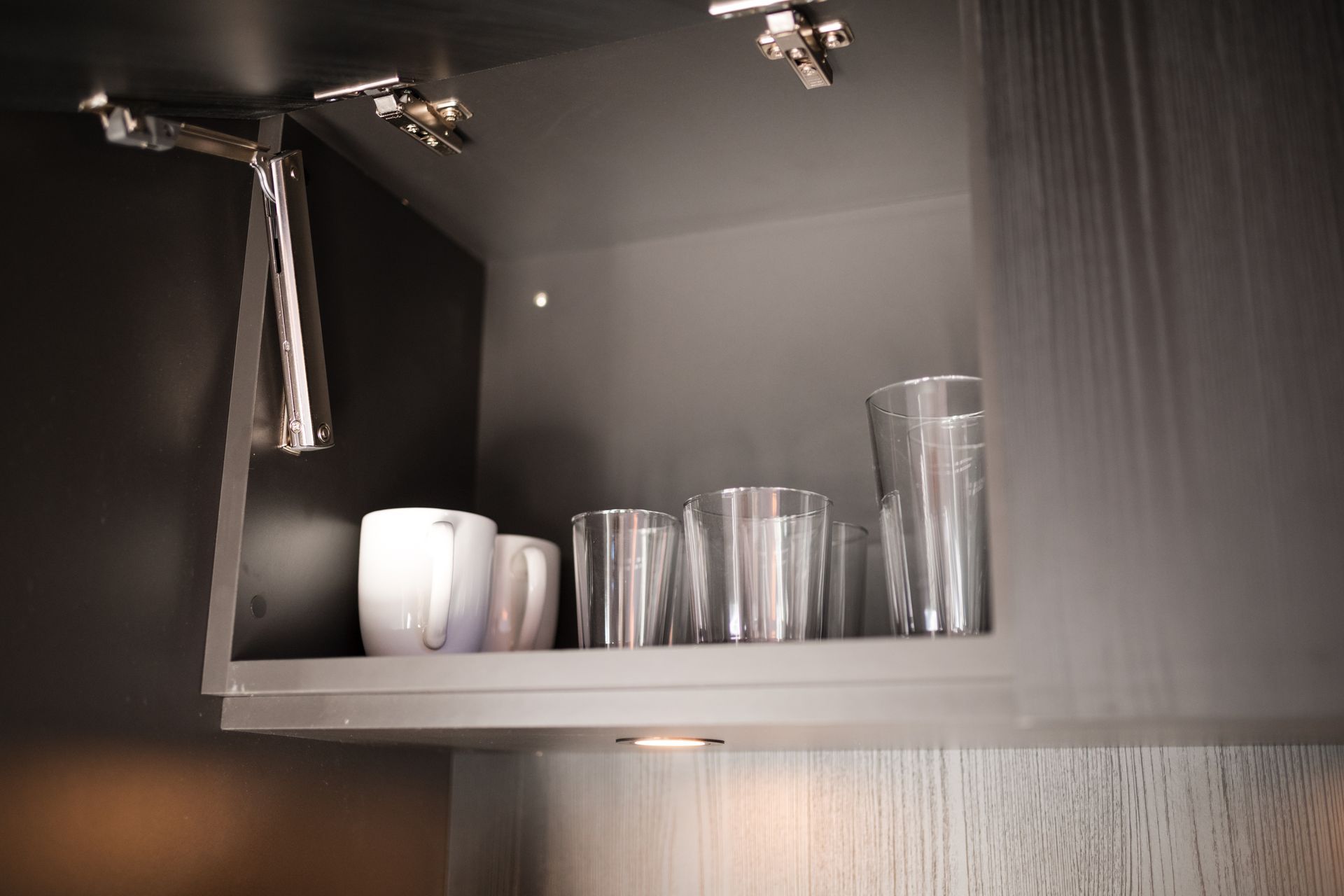 Open cabinet with glasses, mugs, and a towel hanging. Dark gray interior.