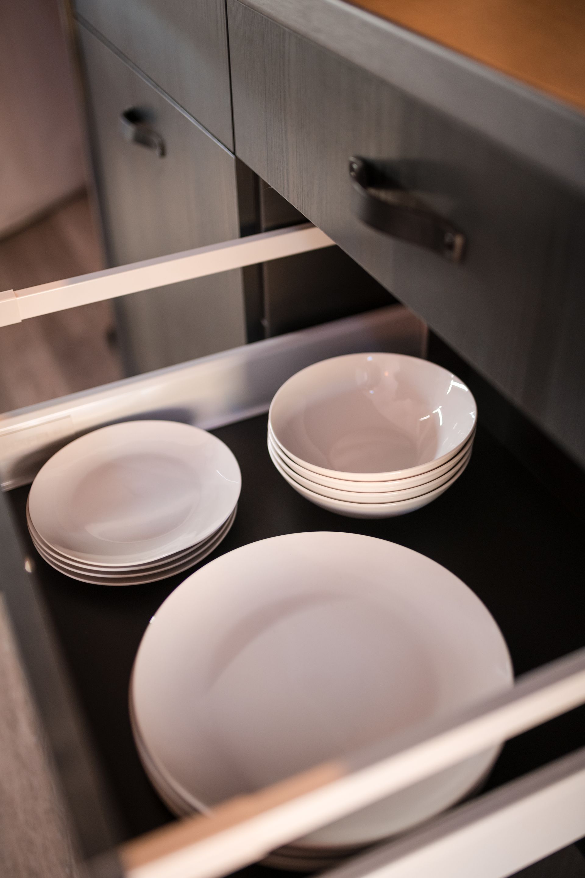 Drawer with white plates and bowls. Dark gray cabinet with light wooden countertop.