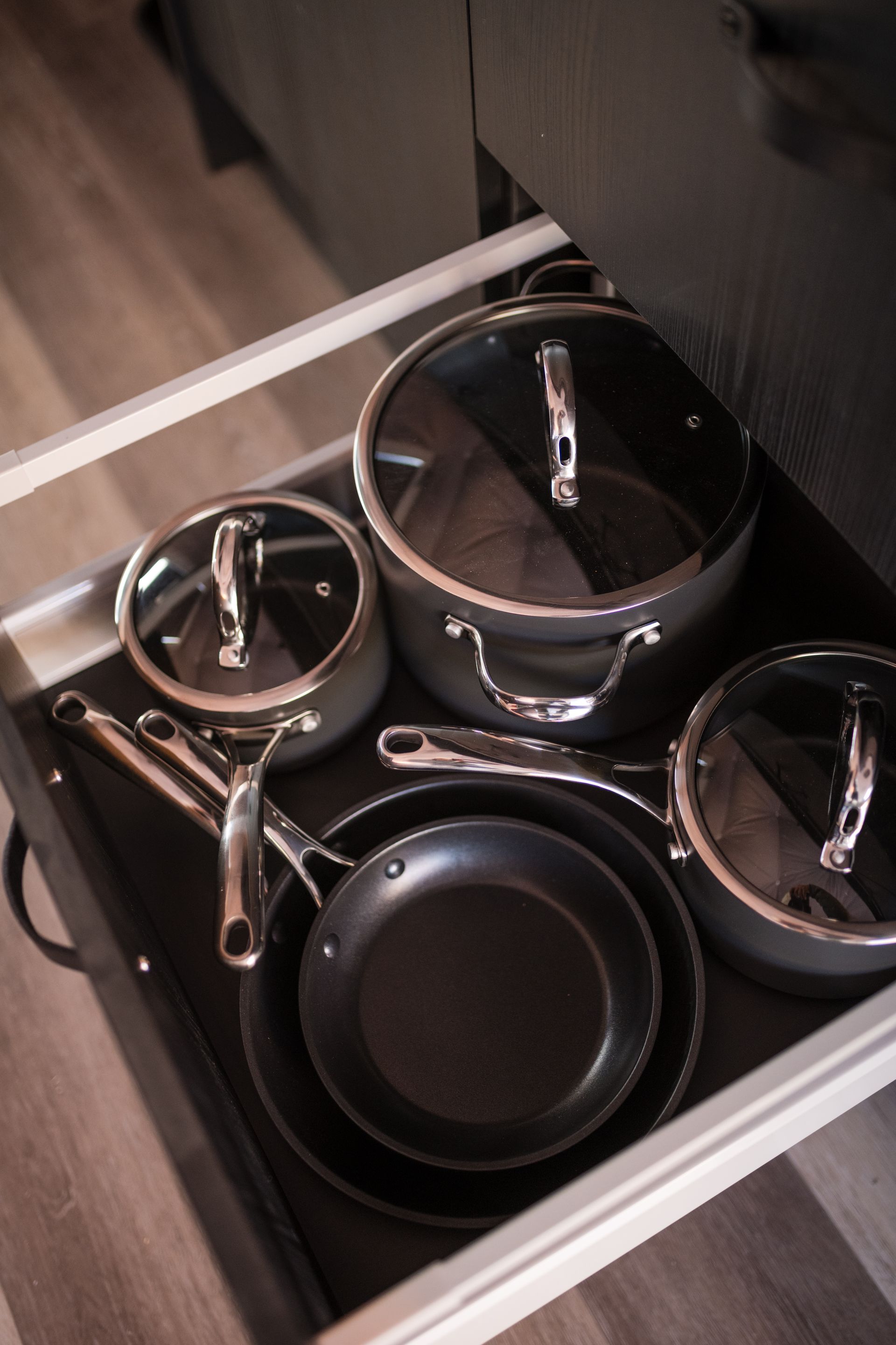 A drawer with cookware: pots, pans, and lids. Gray and black on a black mat.