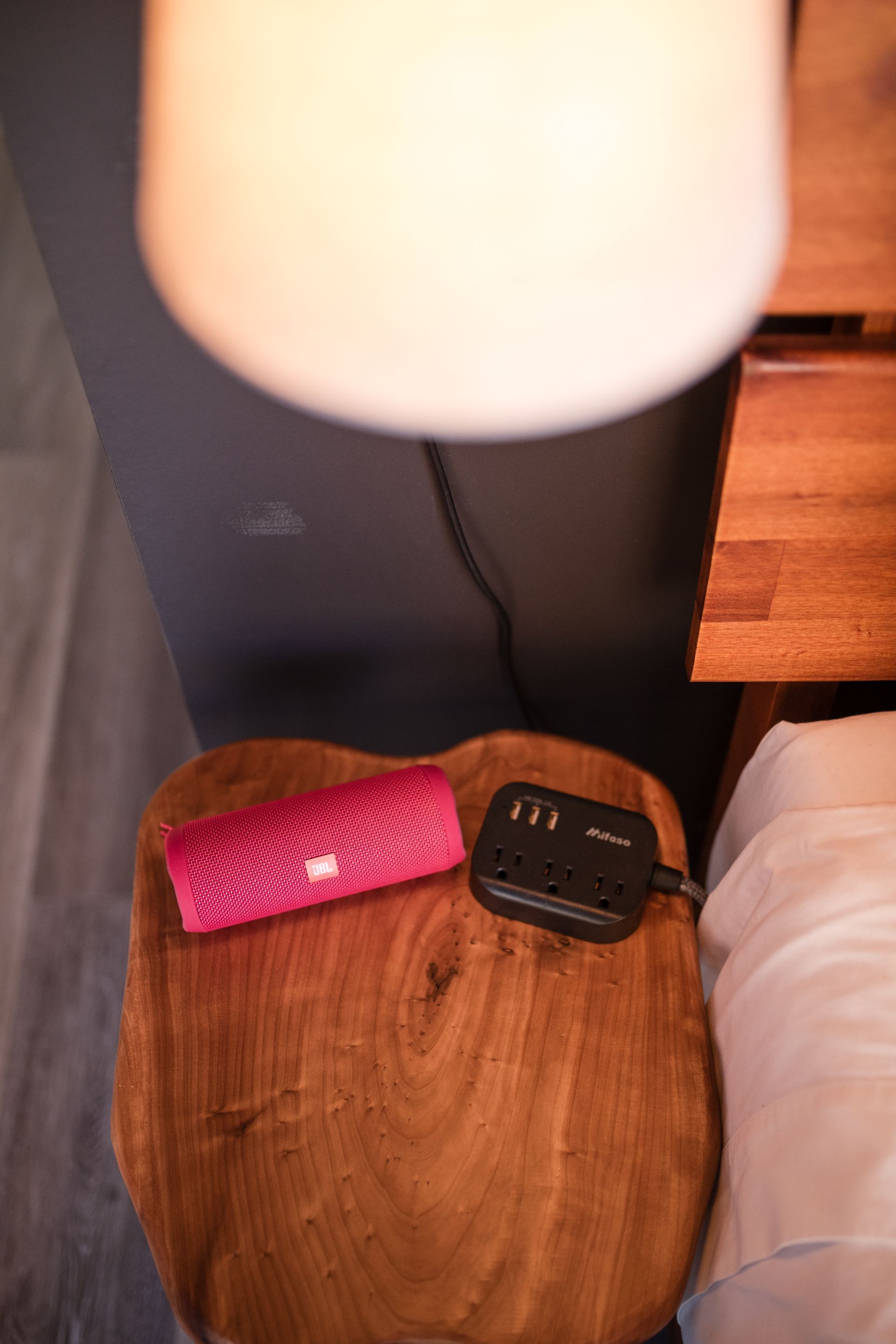 Pink clutch and power strip on a wooden stool, below a lamp.